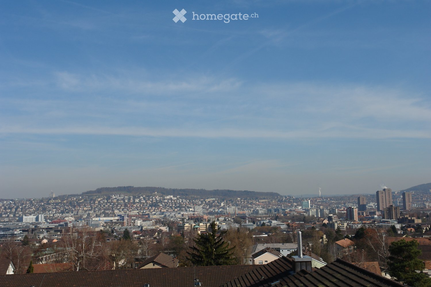 Panoramic cityscape view with a mix of residential and commercial buildings, visible rooftops, and distant skyline.