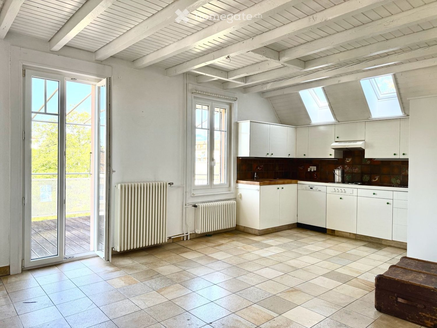 Bright, airy kitchen with white cabinets, a central island, and large windows. The space features tiled flooring and exposed wooden beams on the ceiling.