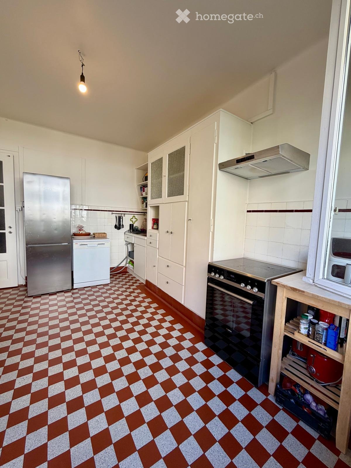 A well-equipped kitchen with white cabinets, stainless steel appliances, and a checkered red and white tile floor.