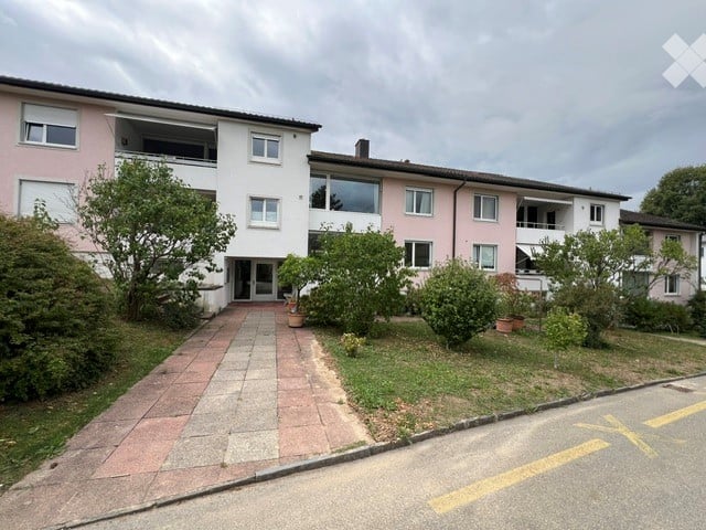 A multi-story residential building with pink and white facades, multiple windows, balconies, and a paved entrance path.