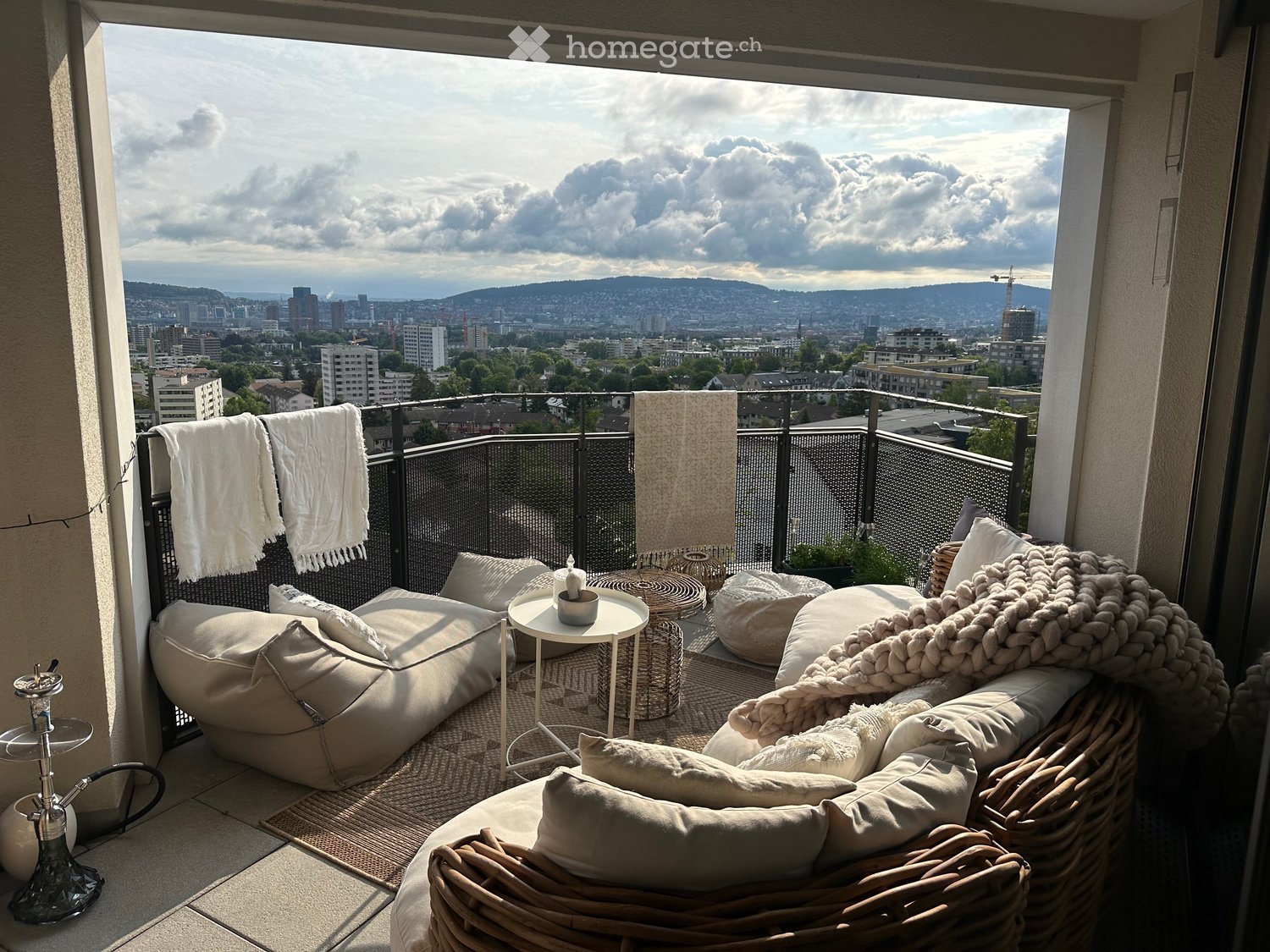 Balcony with cityscape view, featuring a sofa, a small table, and decorative pillows and blankets.