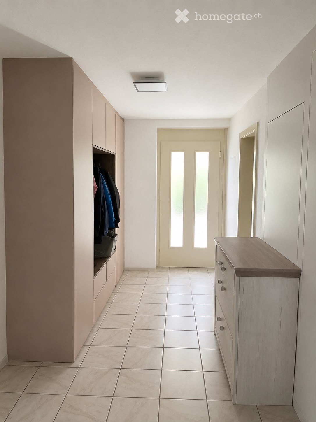 Clean, modern hallway with tiled flooring, built-in storage units, and a double door leading outside.