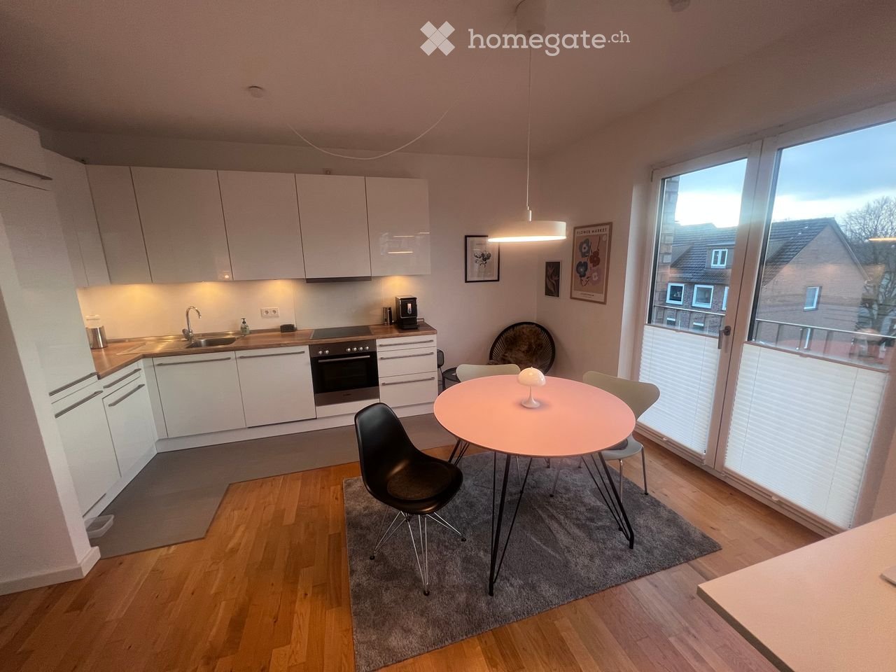 Modern kitchen and dining area with white cabinets, stainless steel appliances, a round dining table with chairs, and a fan near the window.