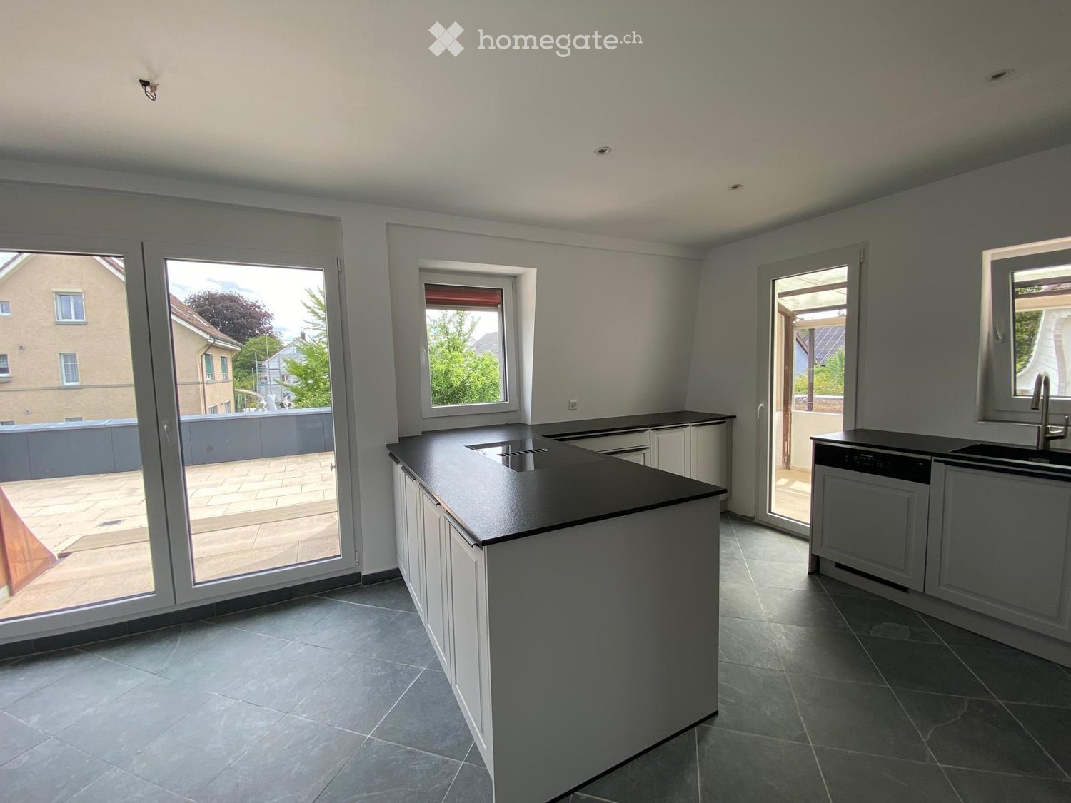 Modern kitchen with white cabinets, black countertops, island, sink, and large windows offering outdoor views.