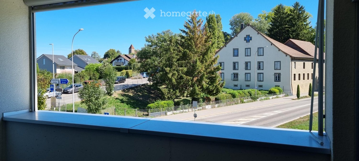 View from a balcony showing a residential street, houses, trees, and a clear blue sky.