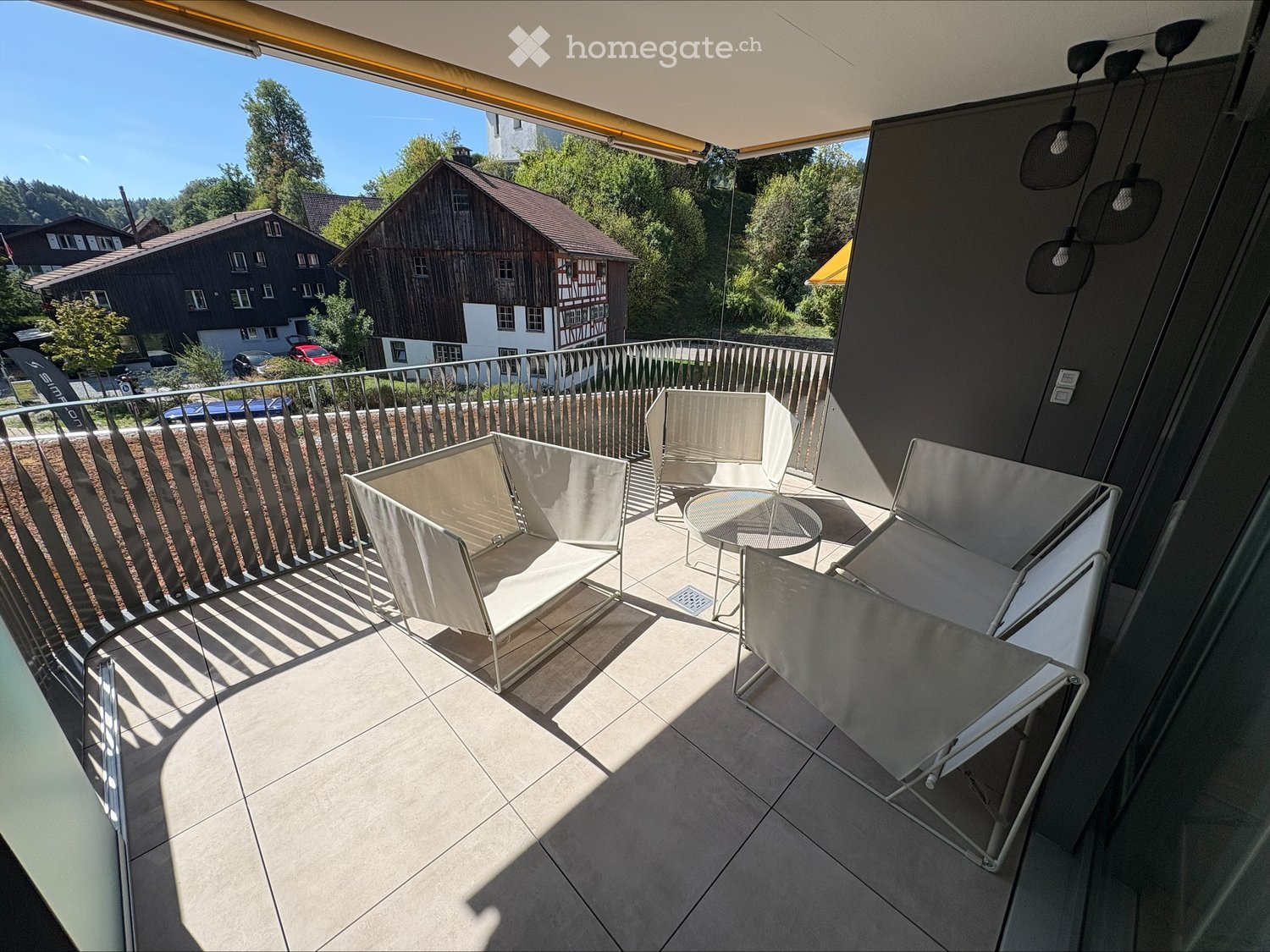Balcony with modern white chairs and a small round table, overlooking a scenic area with houses and trees.
