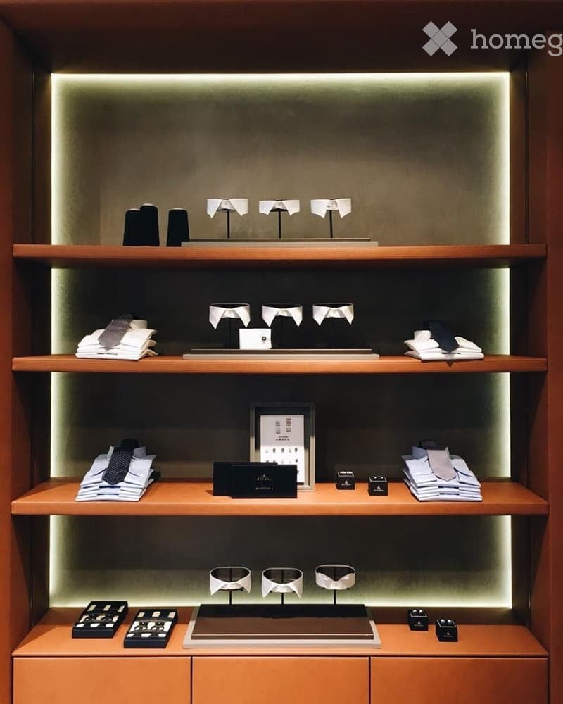 A neatly organized display area with wooden shelves holding folded ties, collar stays, and small boxes, illuminated by soft lighting.