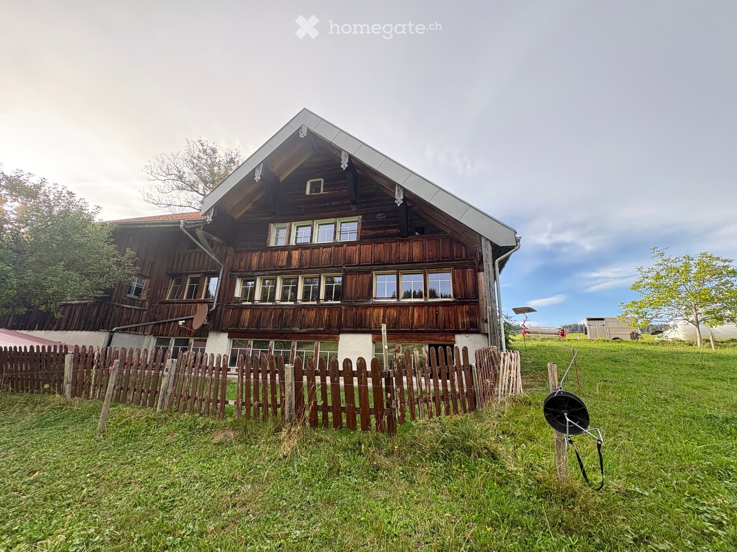 Traditional wooden house with a pitched roof, multiple windows, and a wooden fence surrounding the property.