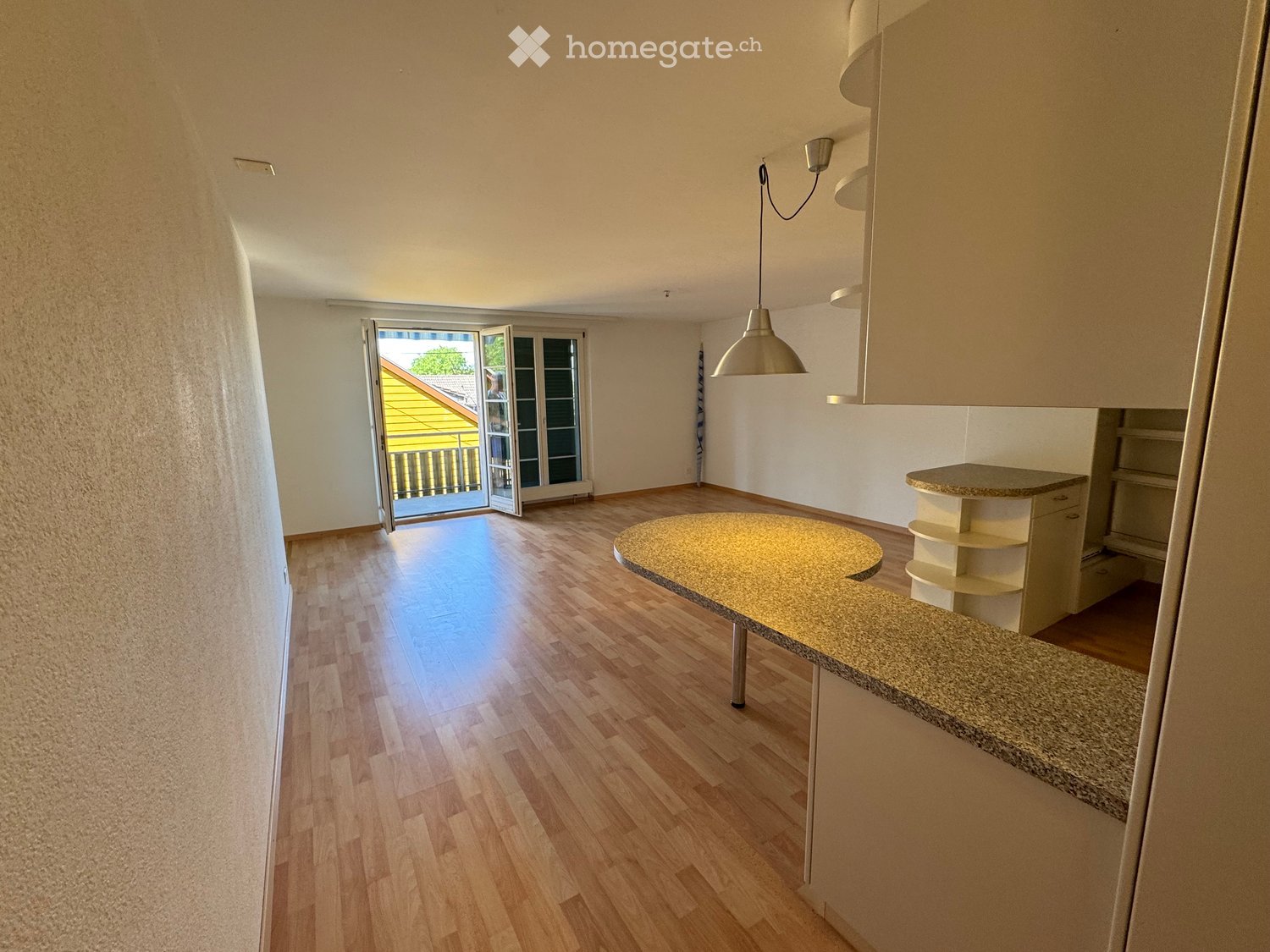 Bright, open room with wooden flooring, a round table, a pendant light, and a cabinet. Large sliding glass doors lead to a balcony.
