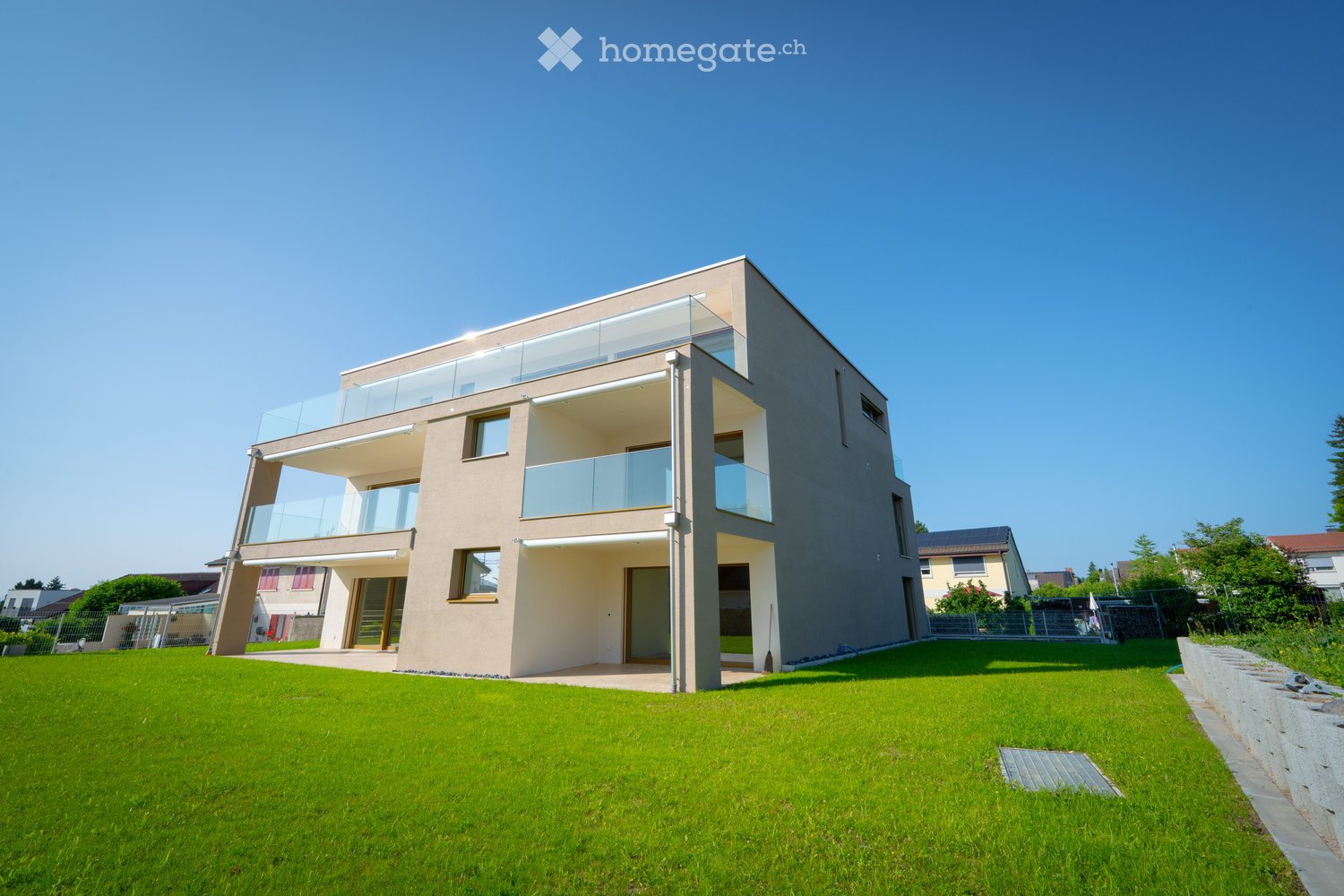 Modern two-story house with large windows and balconies, surrounded by a well-maintained lawn.