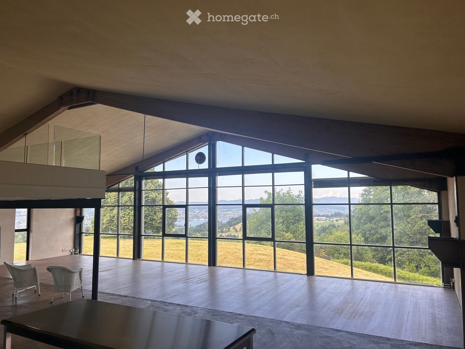 Bright, open room with large windows offering scenic views, wooden floor, and minimal furniture including a table and chairs.