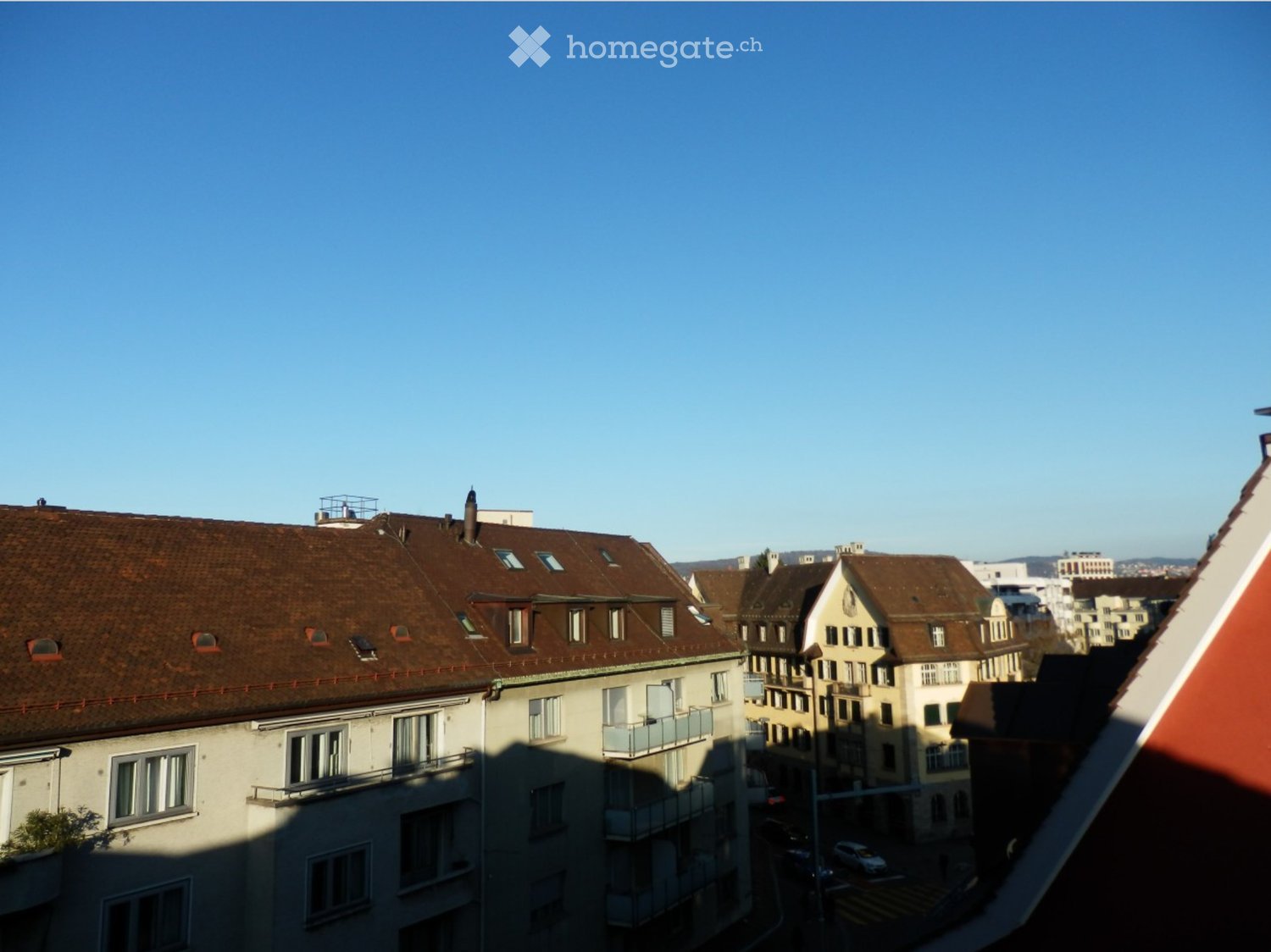 View of a cityscape with multiple residential buildings, featuring brown tiled roofs, windows, and balconies.