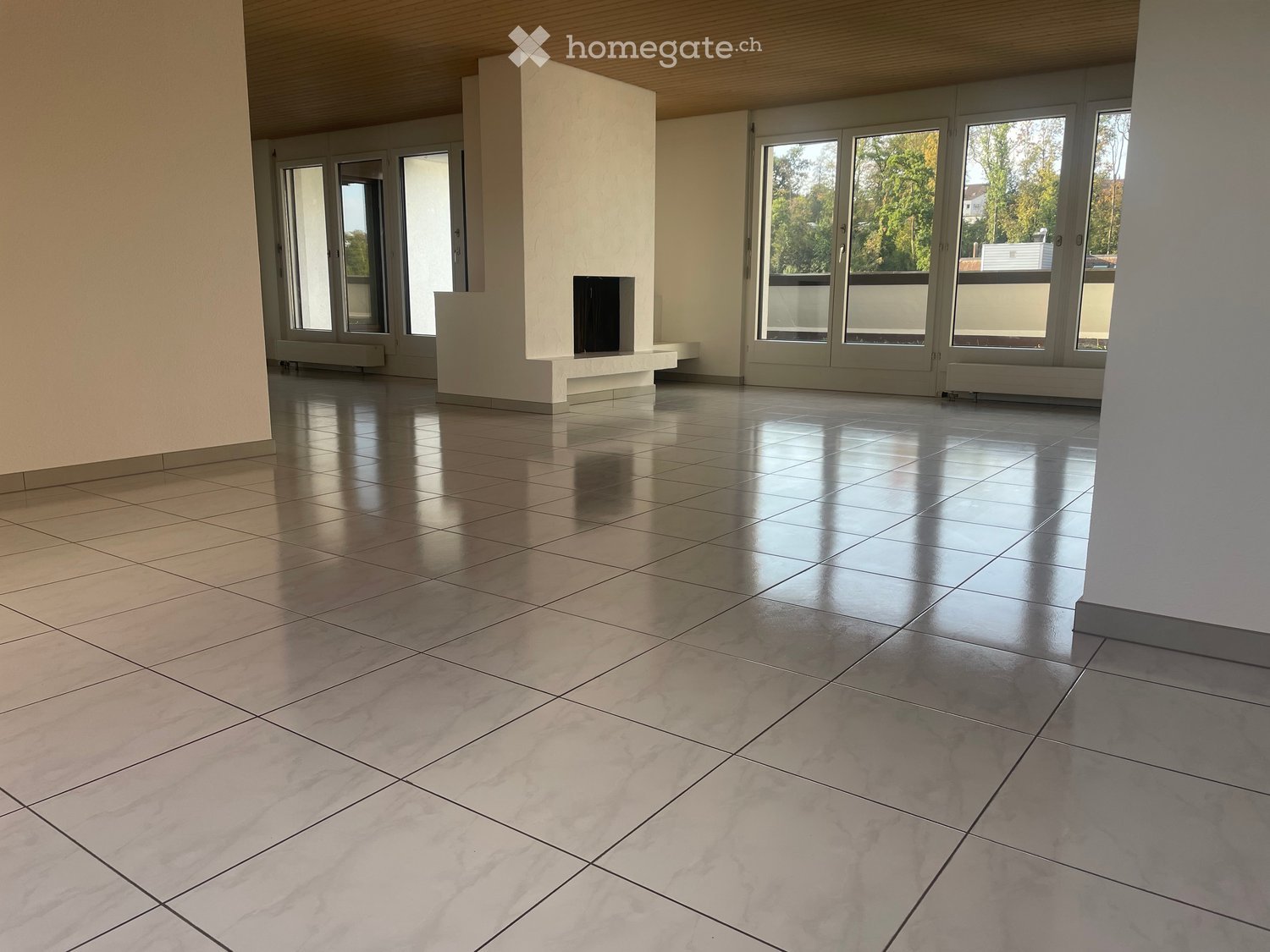 Empty room with polished tile flooring, large windows, and a fireplace area.