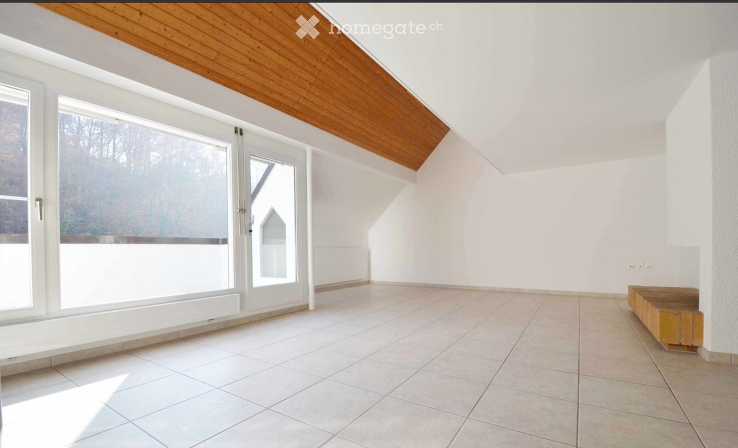 Empty room with white walls, tiled floor, large windows, and a wooden bench in the corner.