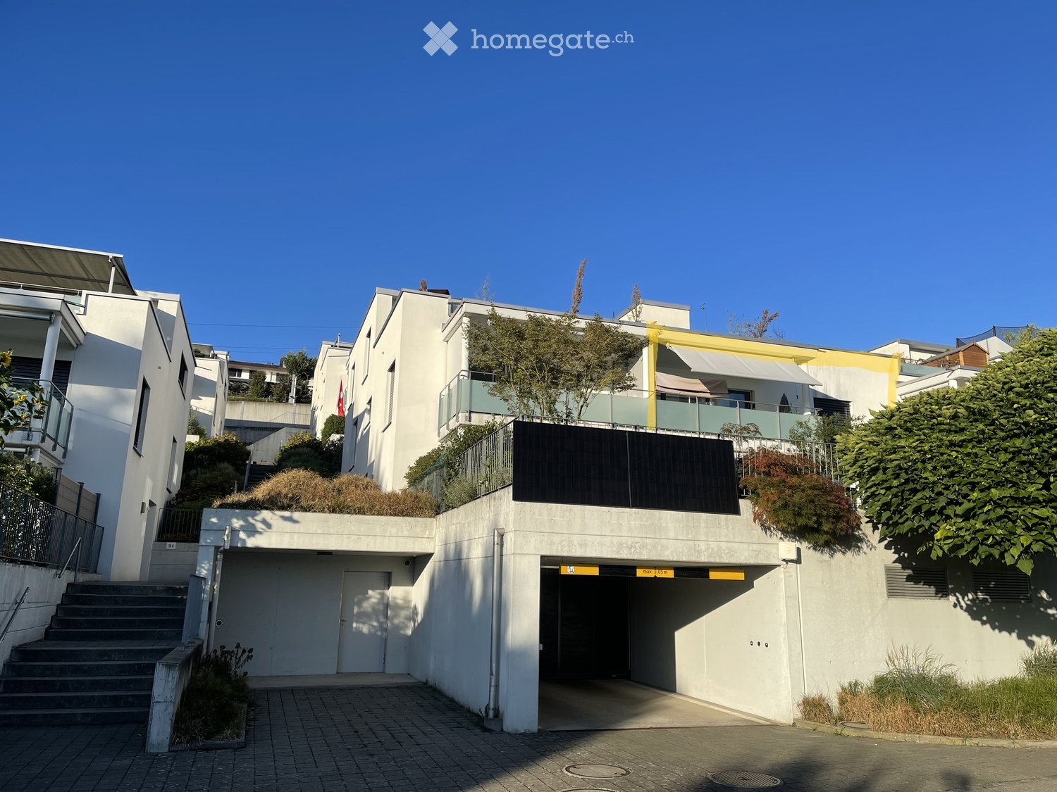 Modern multi-story residential building with white facade, balconies, and a covered parking area.