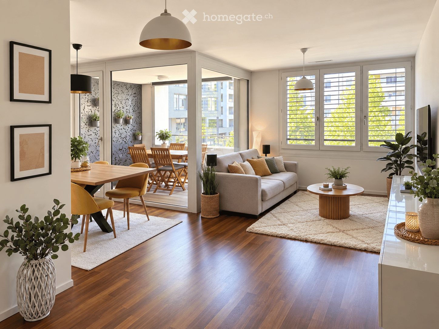 Modern living and dining area with hardwood floors, large windows, a grey sofa, coffee table, dining table with chairs, pendant lights, and decorative plants.