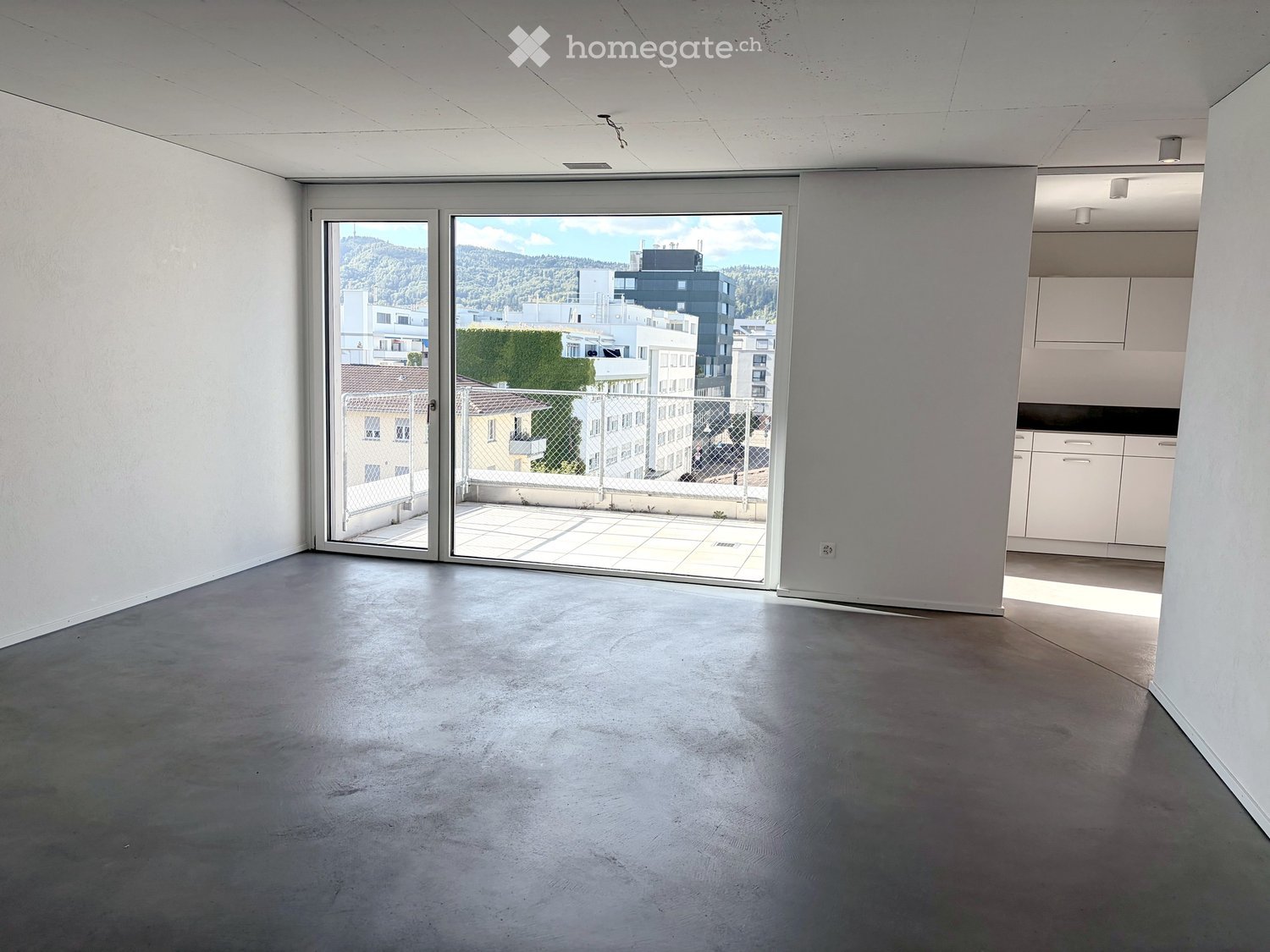 Empty room with concrete floor, white walls, large sliding glass doors leading to a balcony with a city view.