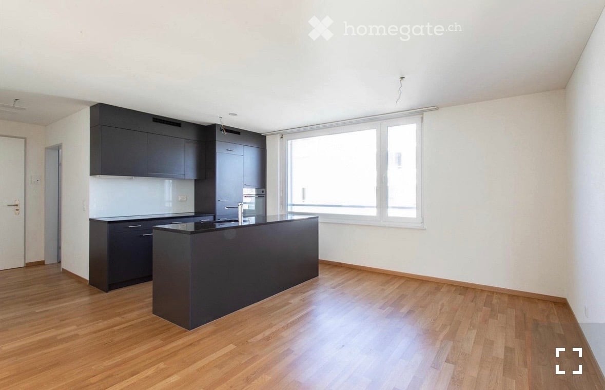 Modern kitchen with dark cabinets, a central island, and a large window, featuring wooden flooring and white walls.