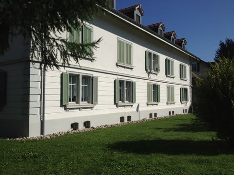 A two-story white house with green shutters and a well-maintained lawn in front.