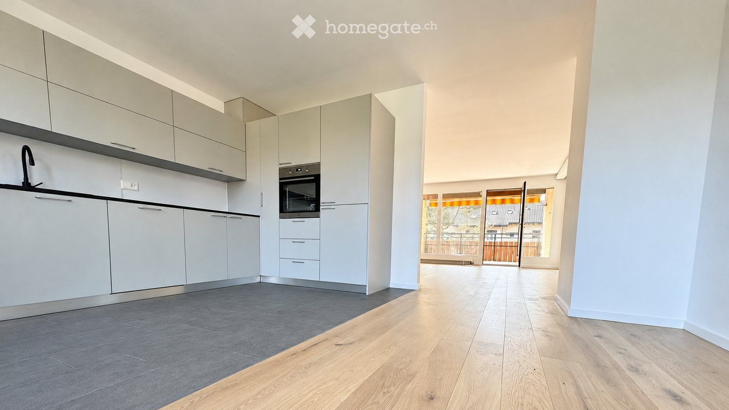 Modern kitchen with white cabinets, grey tiled floor, and wooden flooring extending into the adjacent space.