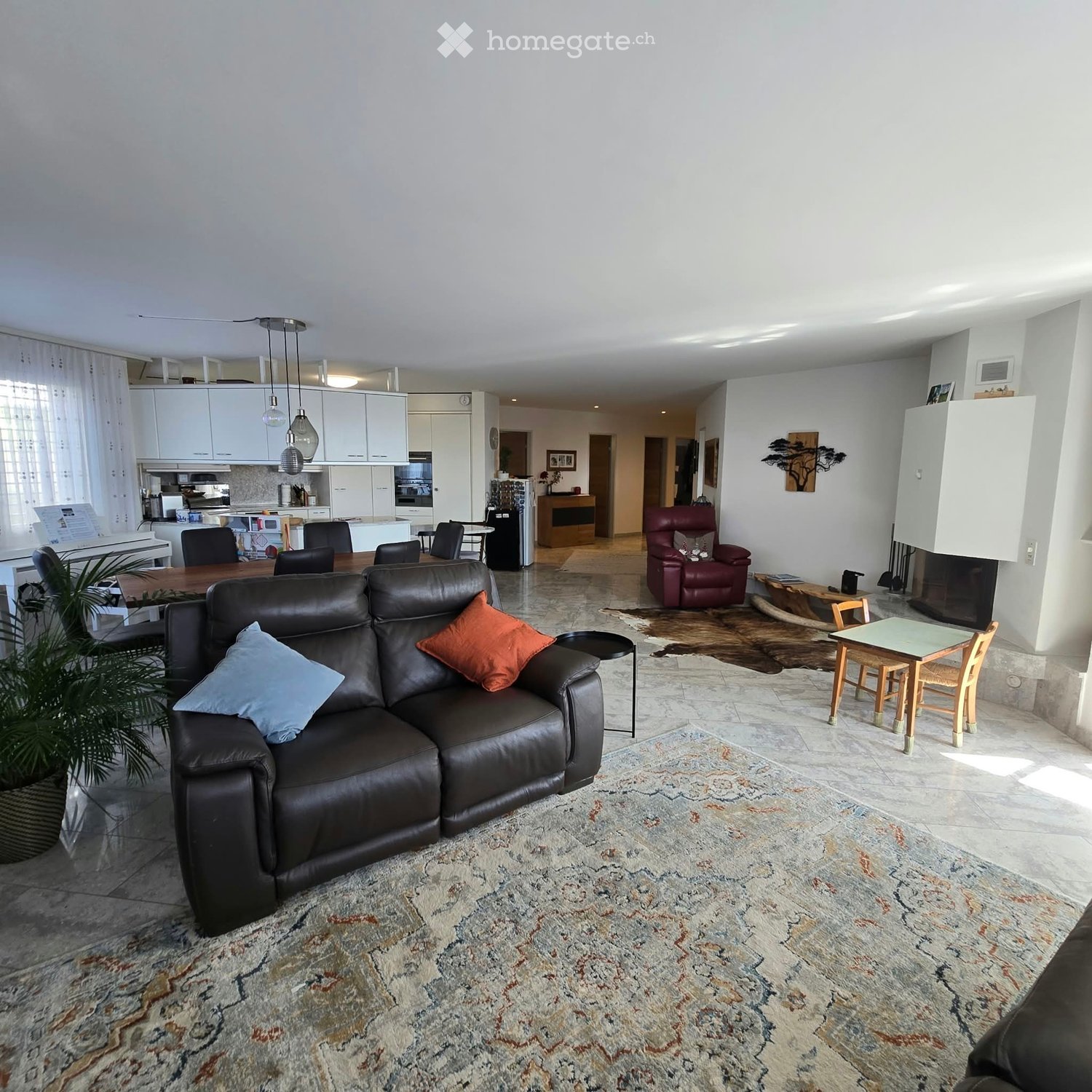 Modern living room with a large leather sofa, coffee table, dining area, kitchen, and fireplace.