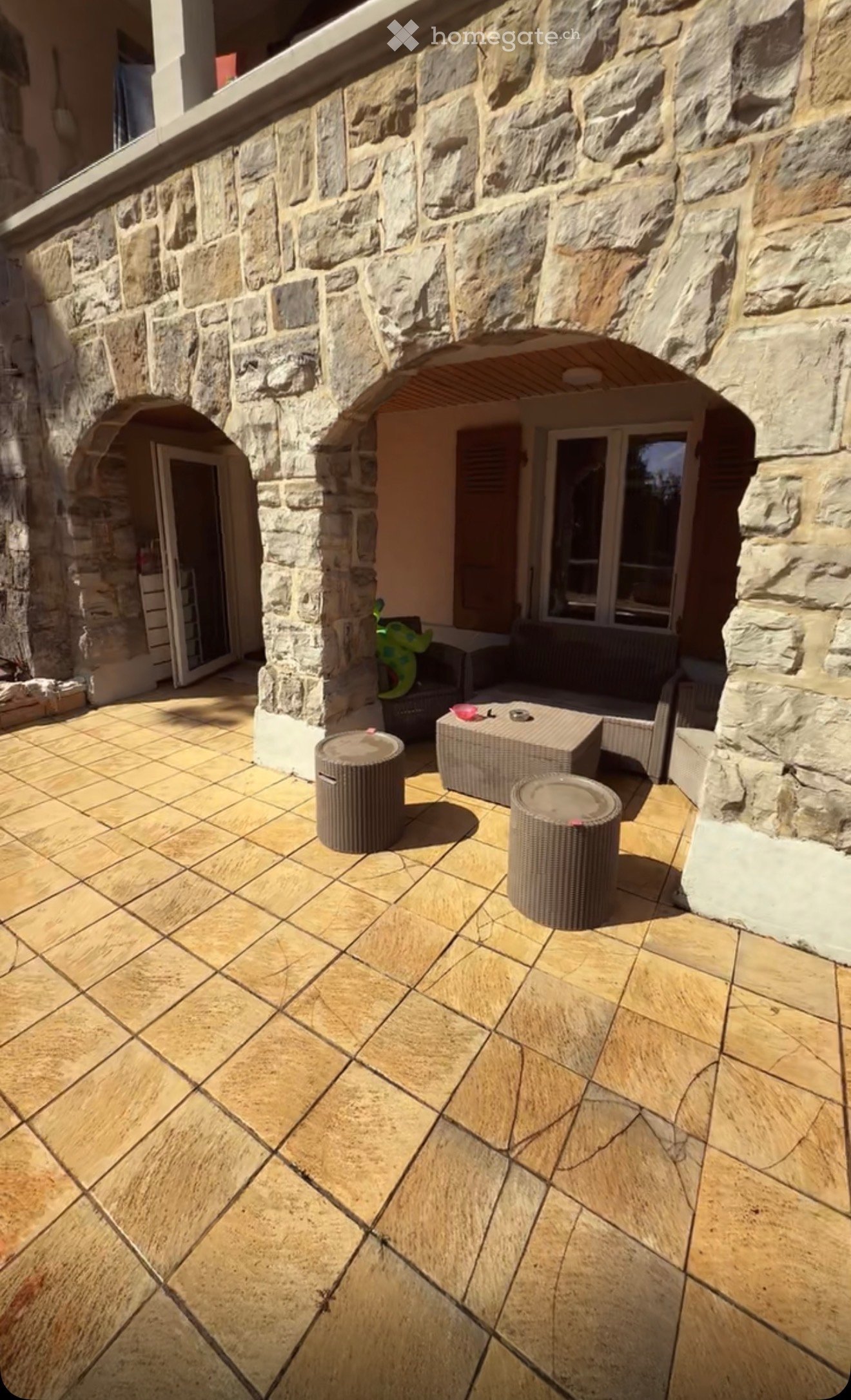 Outdoor patio with stone walls, tiled floor, and outdoor furniture including a table, chairs, and stools.