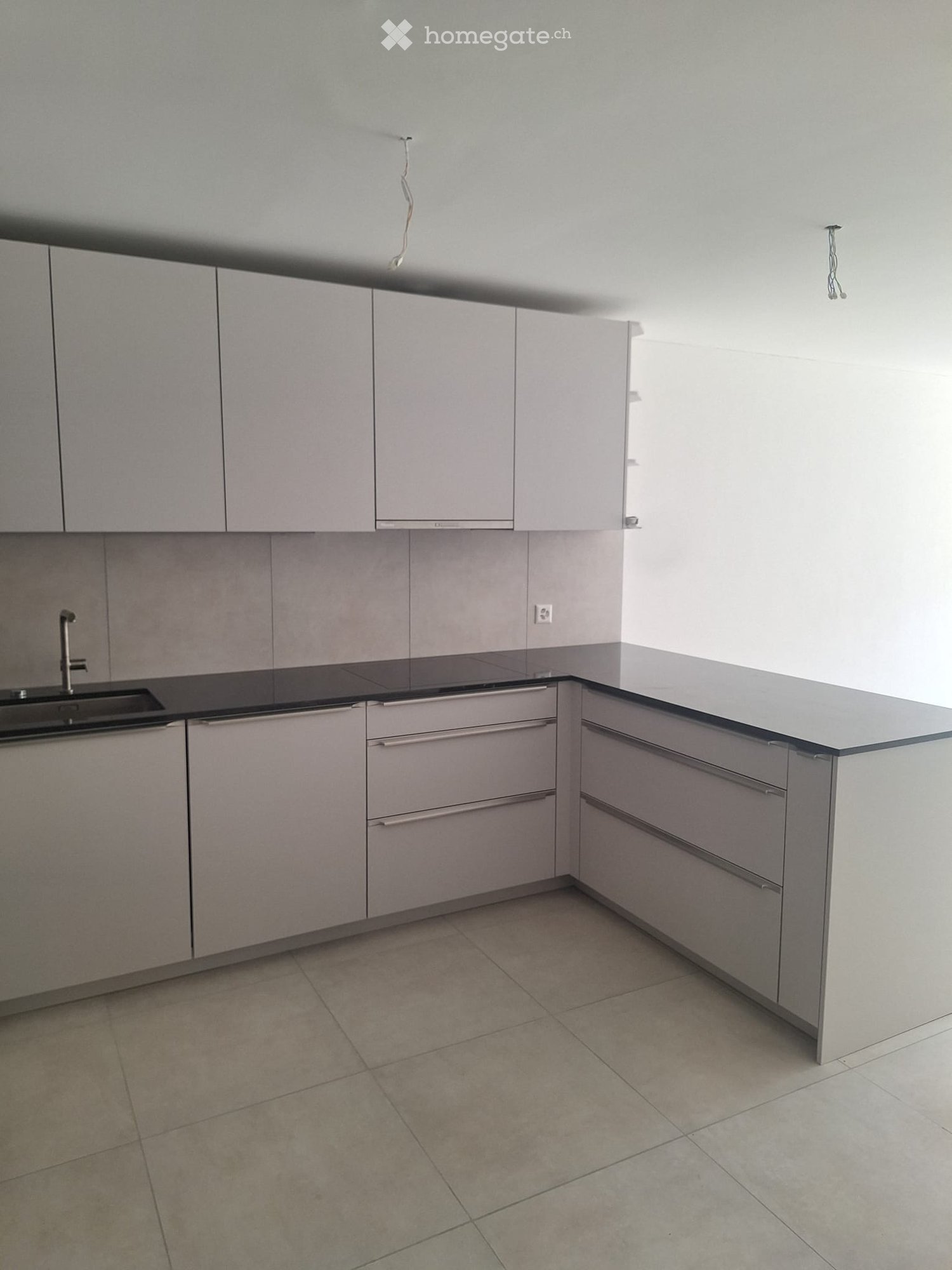 Empty kitchen with grey cabinets, black countertop, and tiled floor. No appliances or furniture present.