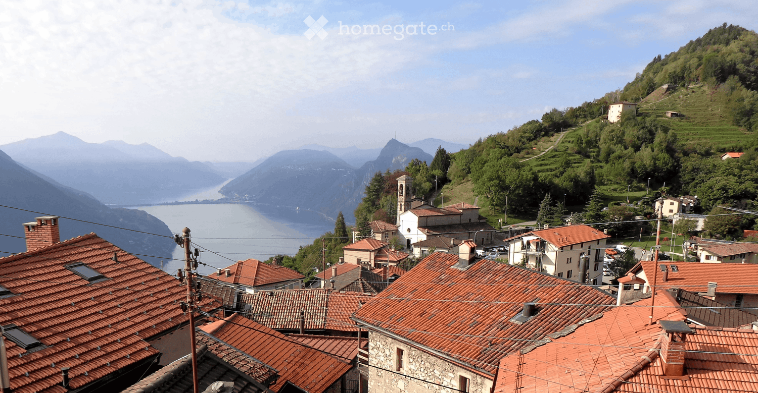 A picturesque village with red-tiled roofs, nestled in a valley surrounded by mountains and a lake.