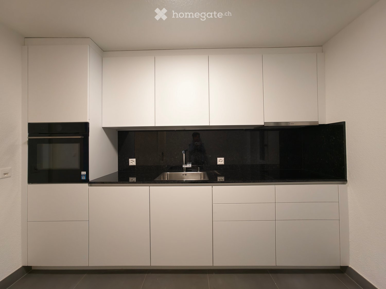 Modern kitchen with white cabinets, black countertop, stainless steel sink, and built-in oven.