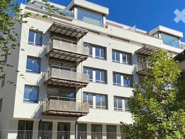 Modern multi-story apartment building with white facade, large windows, and multiple balconies.