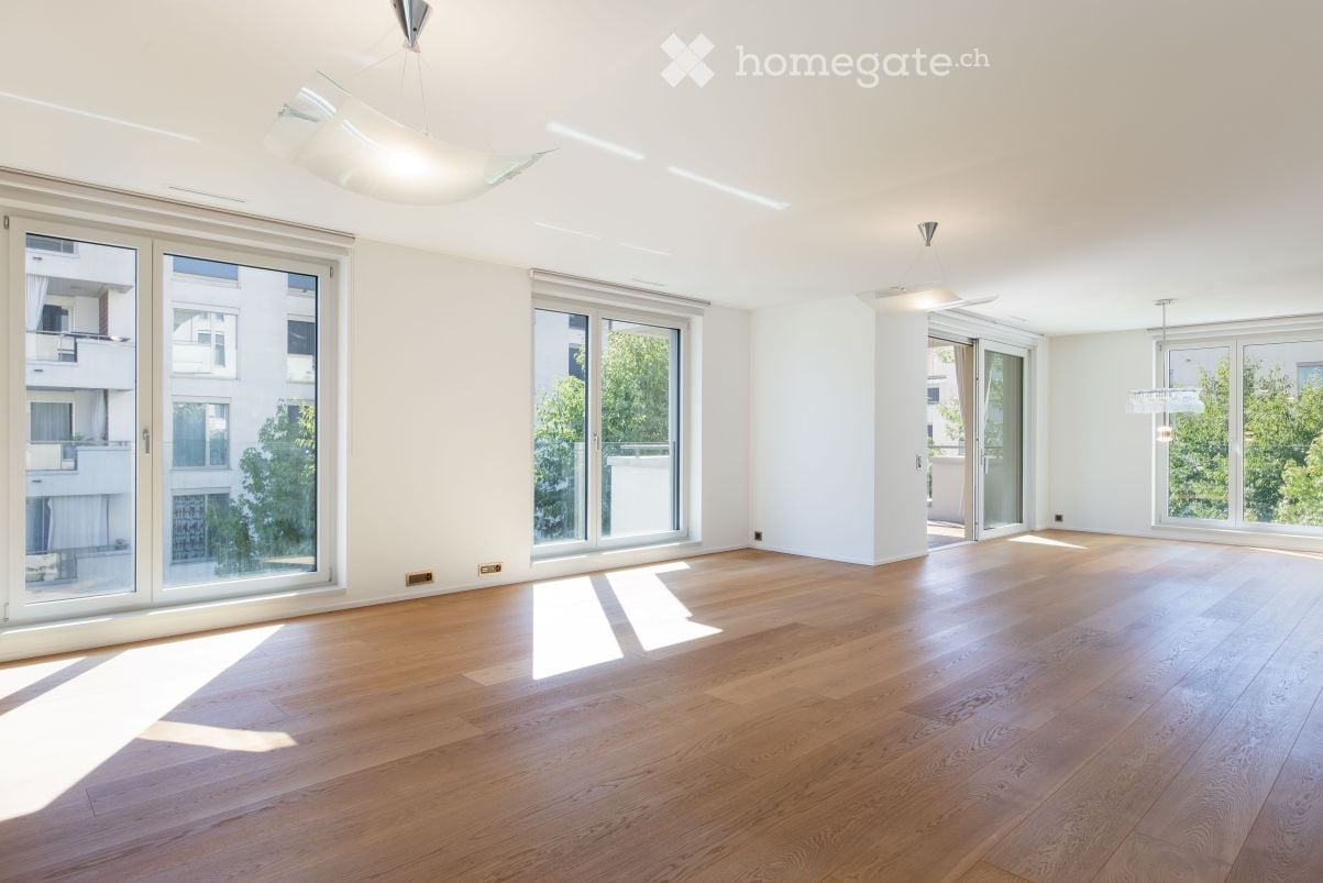 Empty room with wooden flooring, large windows, and modern ceiling lights.