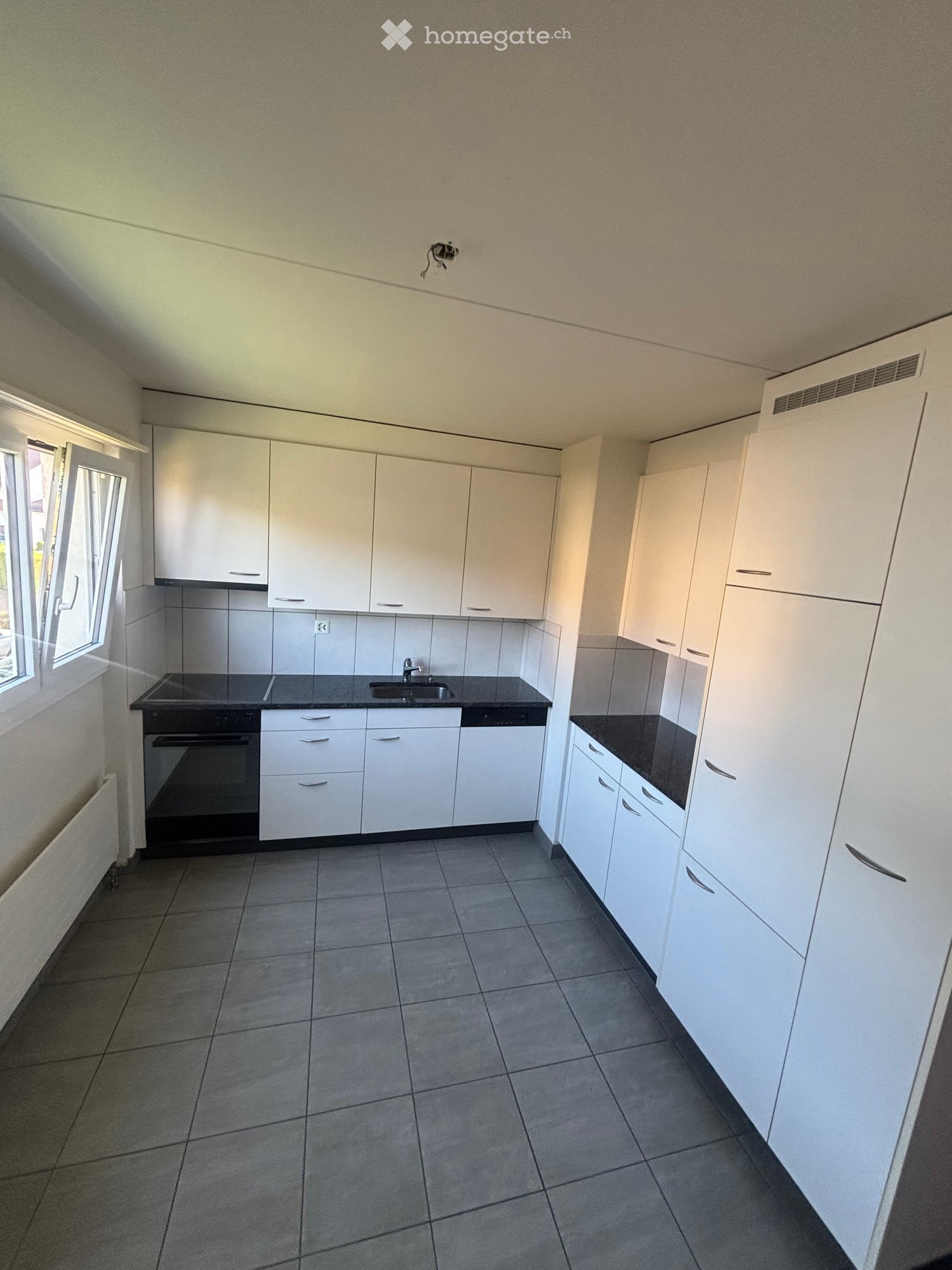 Empty kitchen with white cabinets, black countertops, and tiled flooring. Features include a sink, stove, and built-in oven.