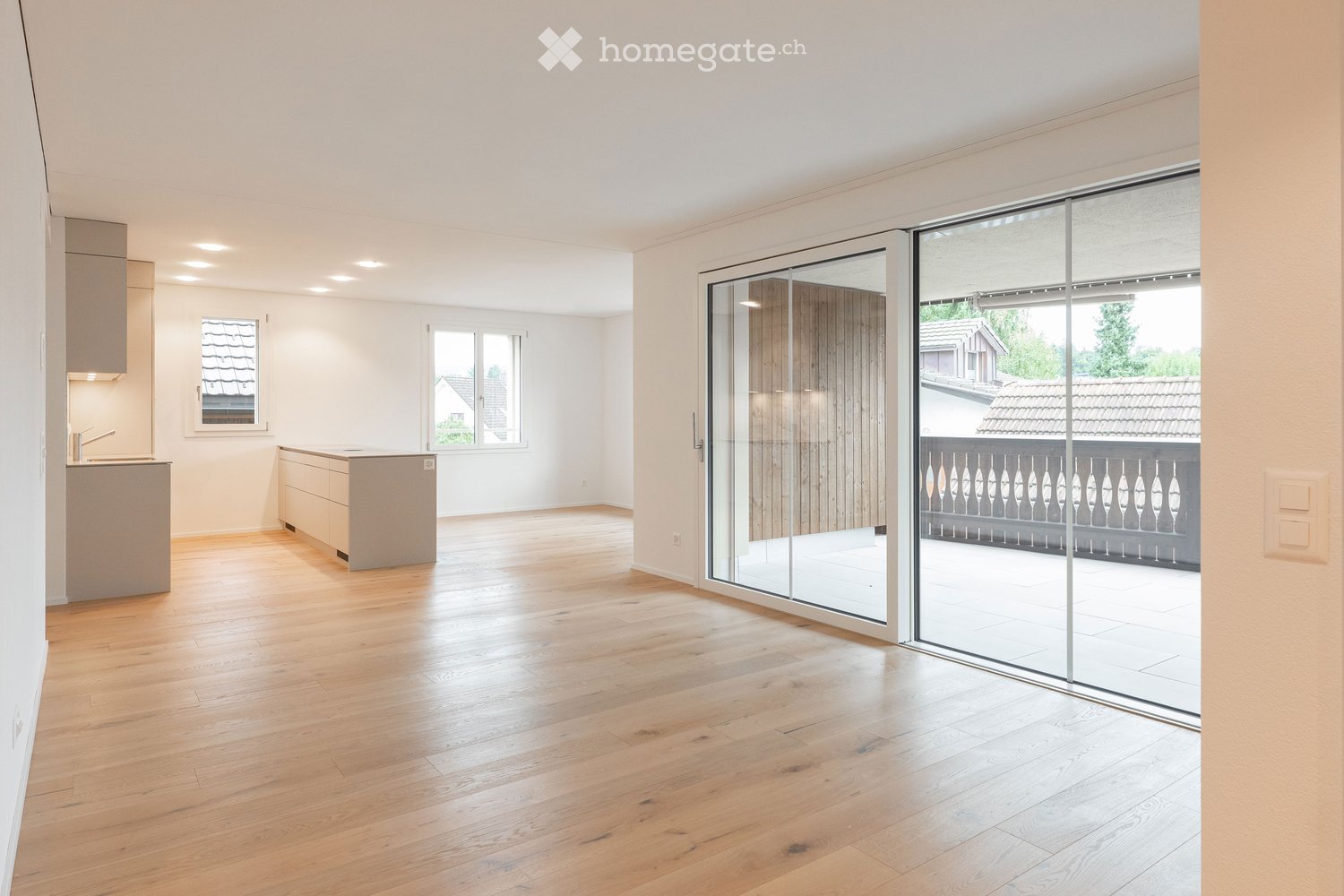 Bright, unfurnished room with wooden flooring, large windows, and a sliding glass door leading to a balcony.