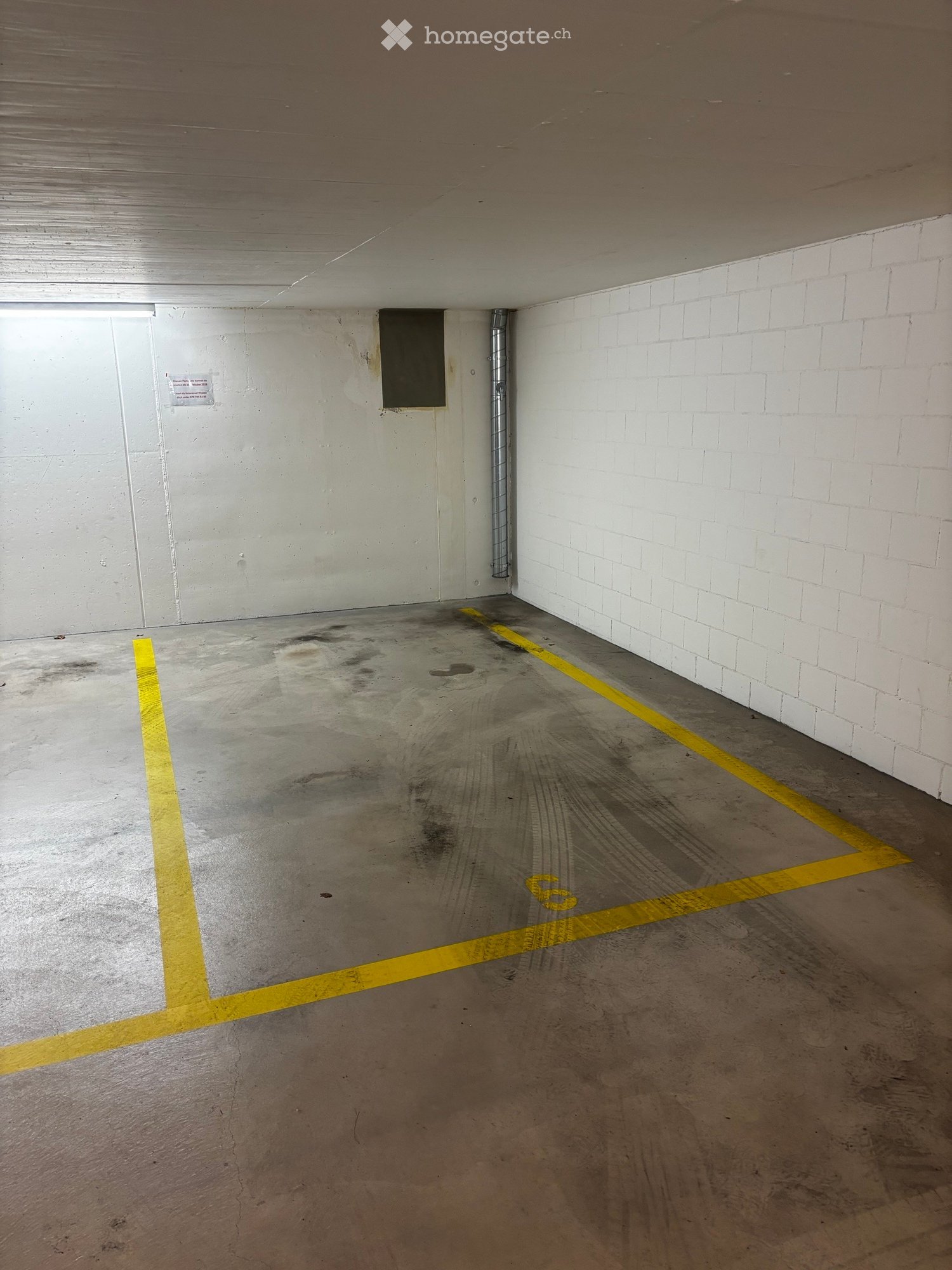 Empty underground parking space with concrete floor, white brick walls, and yellow parking lines.