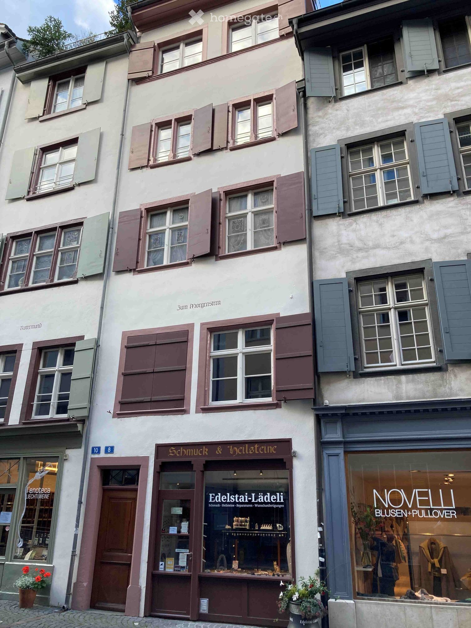 Three-story building with multiple windows, shutters, and storefronts including a jewelry store and clothing store.