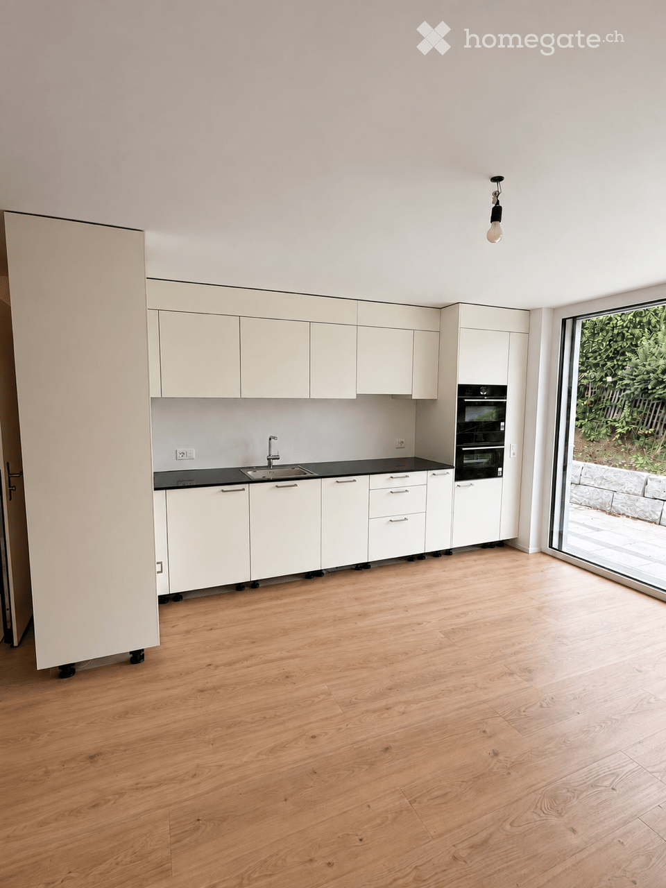 Modern kitchen with white cabinets, black countertops, wooden flooring, and a large window overlooking a garden.