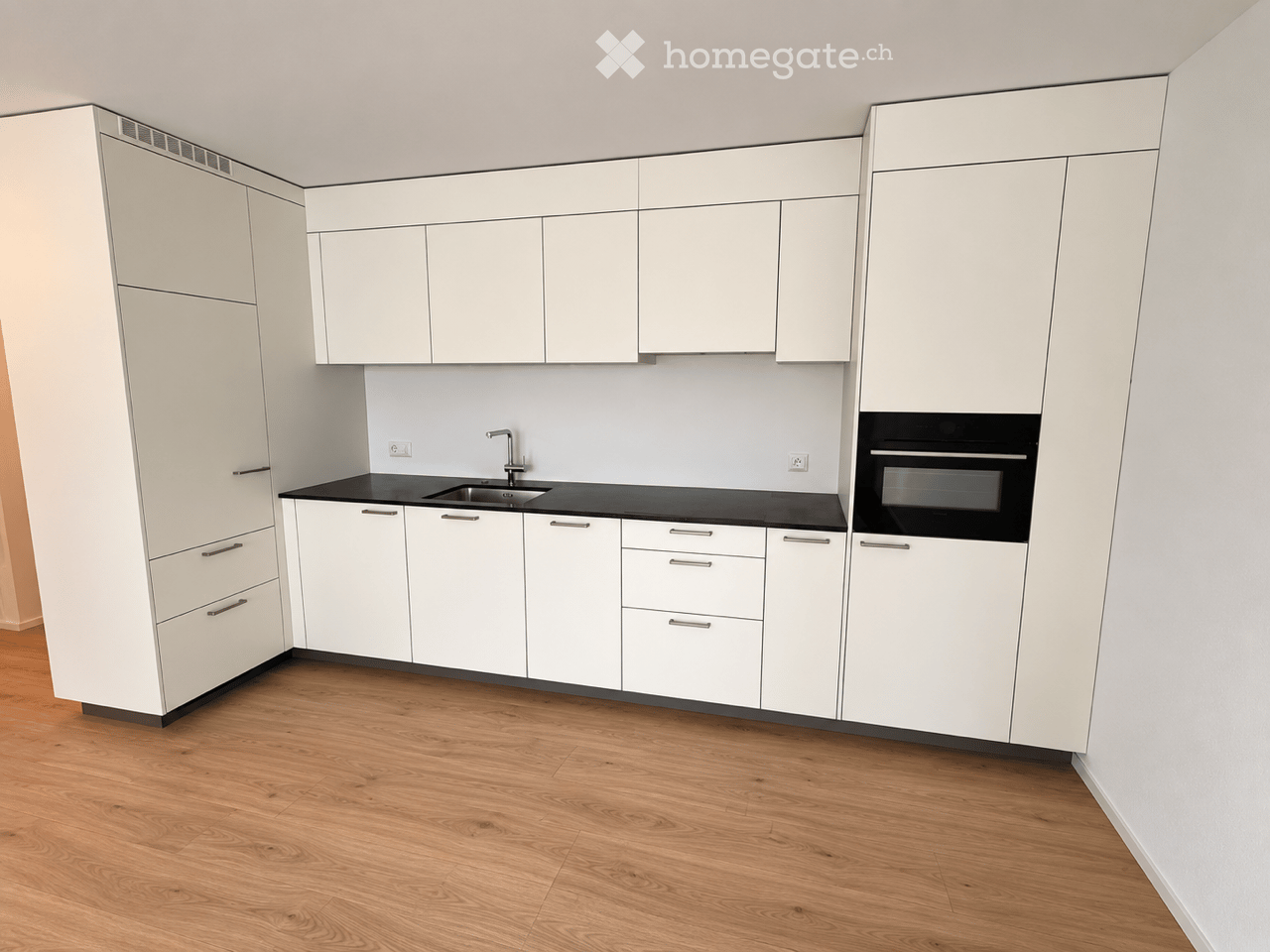 Modern kitchen with white cabinets, black countertops, and a stainless steel sink and faucet. The floor is made of light wood.
