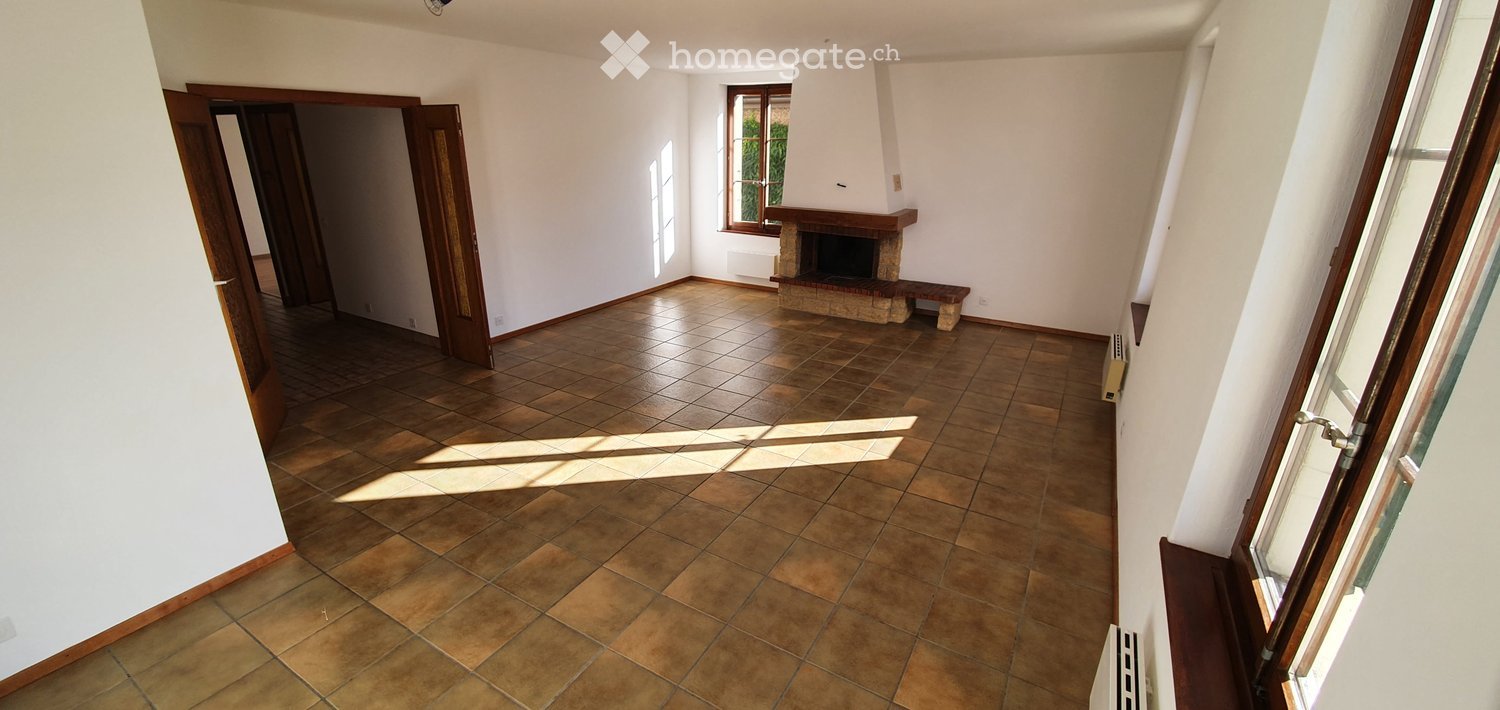 Empty room with tiled floor, white walls, fireplace, and large windows allowing natural light.