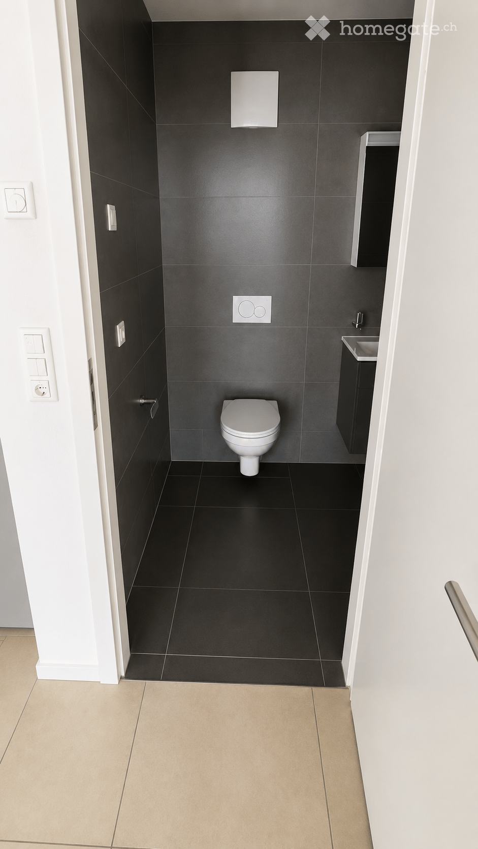 Modern bathroom with black tiled walls and floor, white toilet, sink, and mirror.
