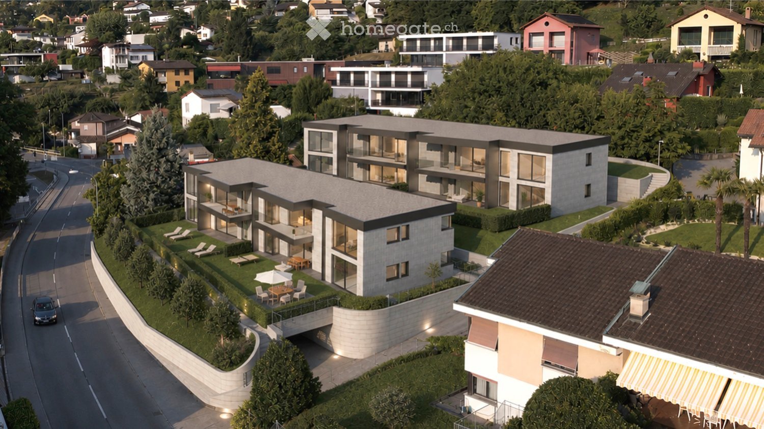 Aerial view of a modern multi-story residential building with large windows, balconies, and a landscaped garden area with outdoor furniture.