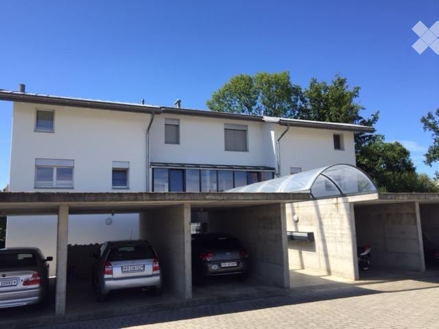 Two-story white building with a covered garage area containing three parked cars.