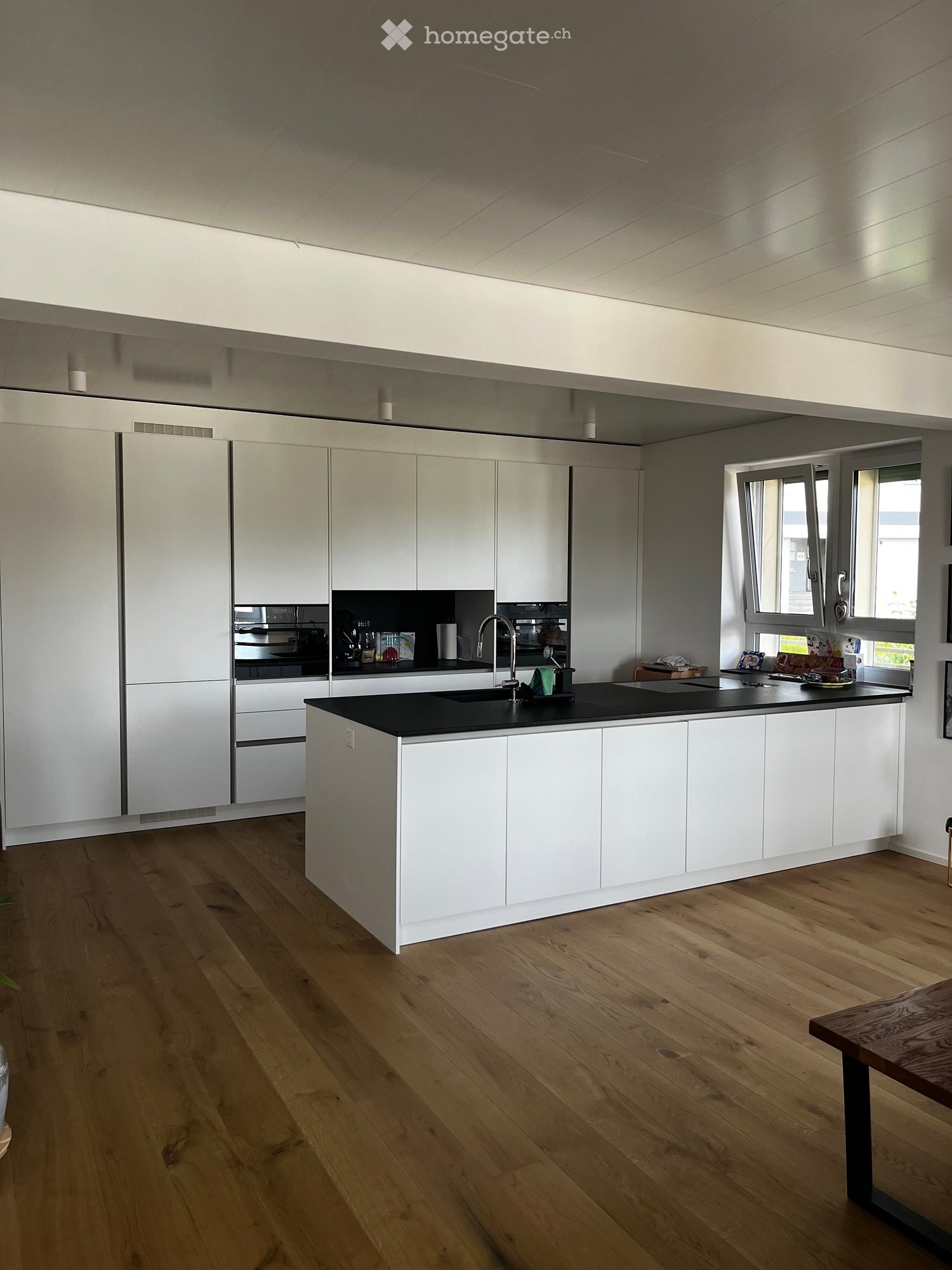 Modern kitchen with white cabinets, black countertop, wooden flooring, and a central island.