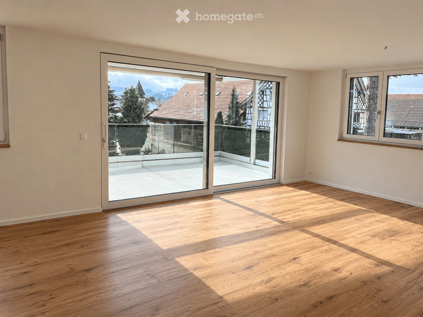 Empty room with wooden flooring, large sliding glass doors leading to a balcony, and a window on the right side.