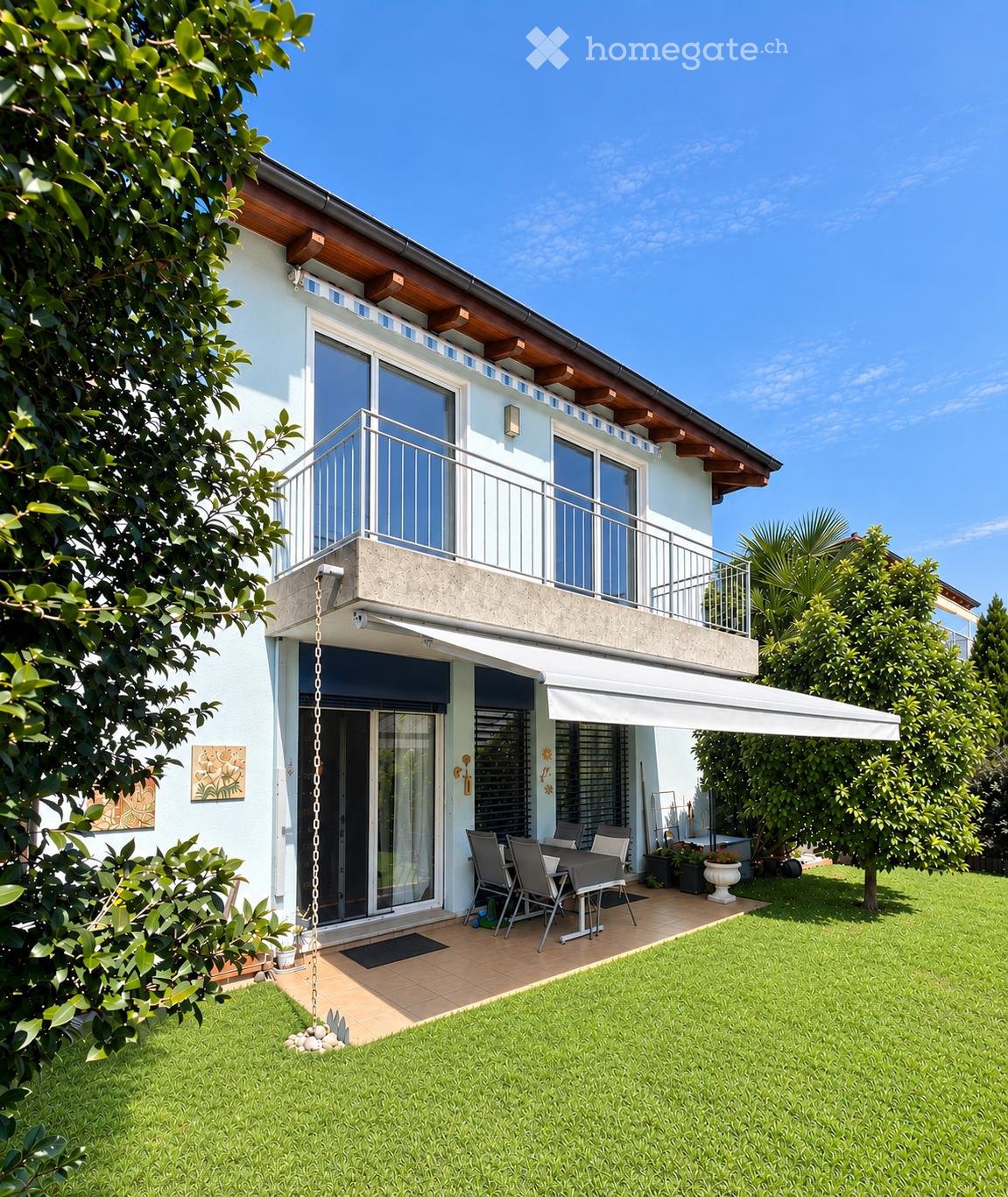 Two-story house with a balcony, patio area, and outdoor furniture.