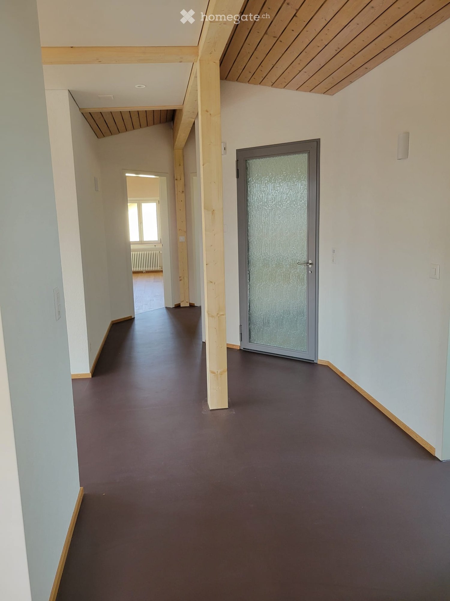 Empty hallway with wooden beams, brown floor, glass door, white walls, wooden trim