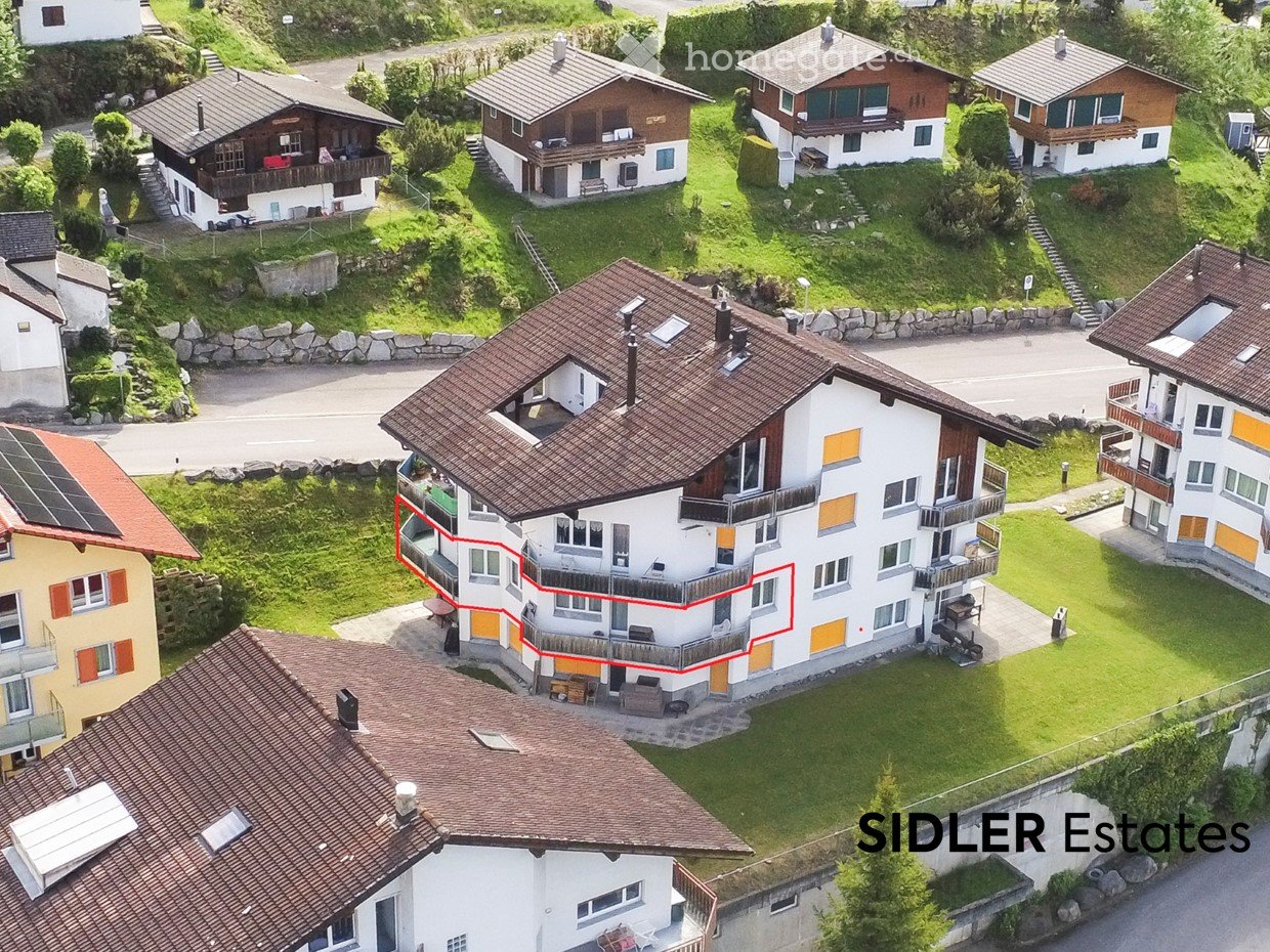 Aerial view of a multi-story residential building with balconies, surrounded by other houses and greenery.