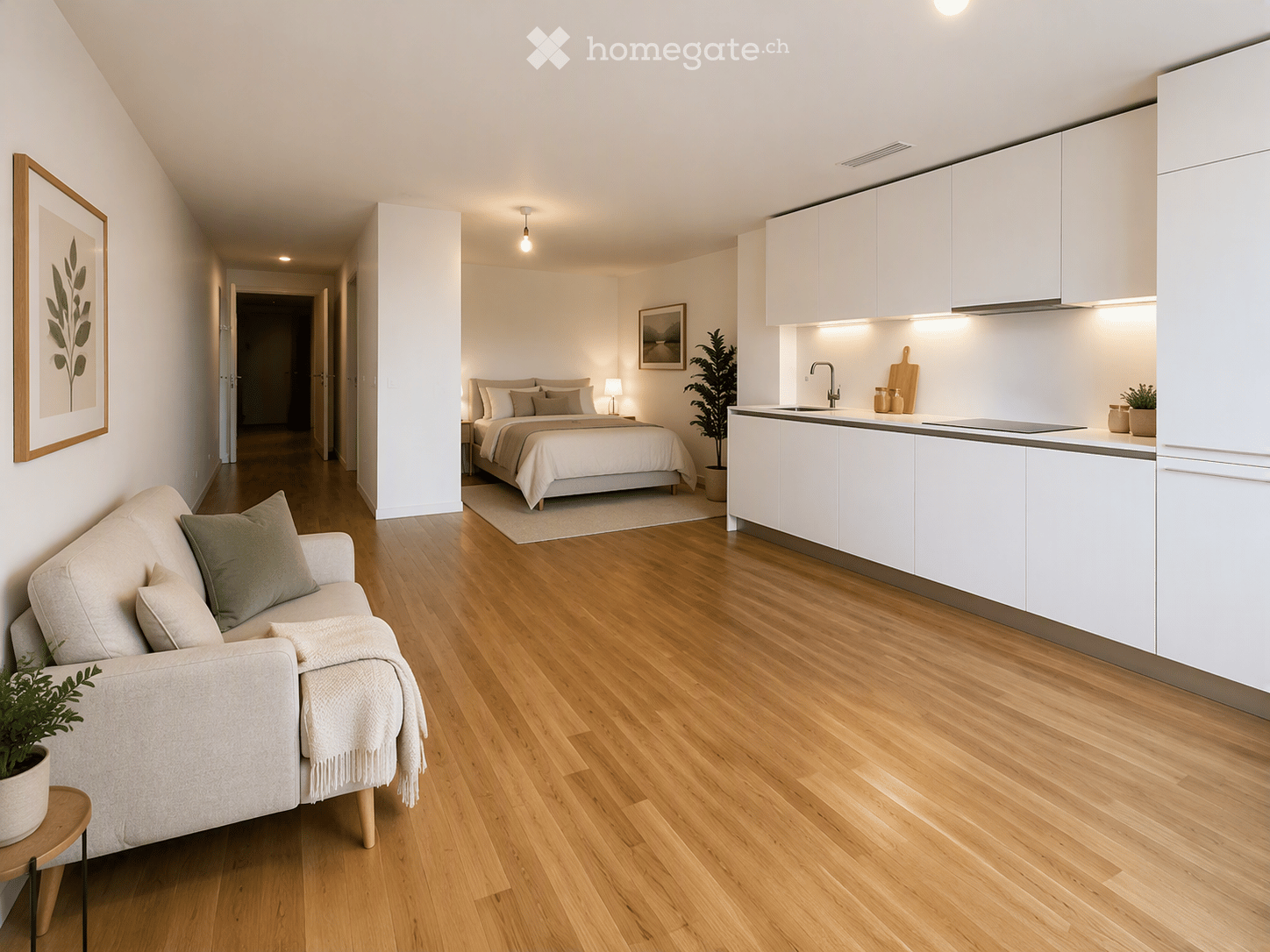 Modern, open-concept living space with a light-colored sofa, a neatly made bed, and a sleek white kitchen area. The room features light wooden flooring, white walls, and contemporary decor including framed artwork and potted plants.