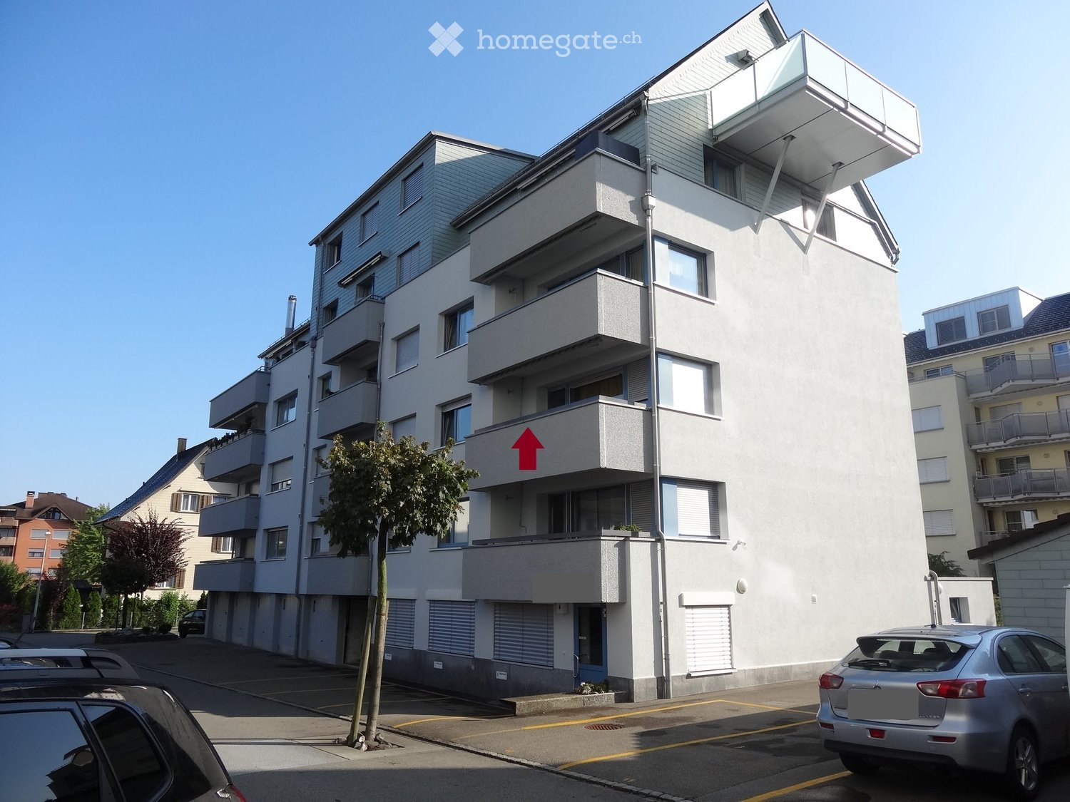 Modern multi-story apartment building with balconies, large windows, and a sleek design. The building features a contemporary architectural style with clean lines and a combination of white and grey tones.