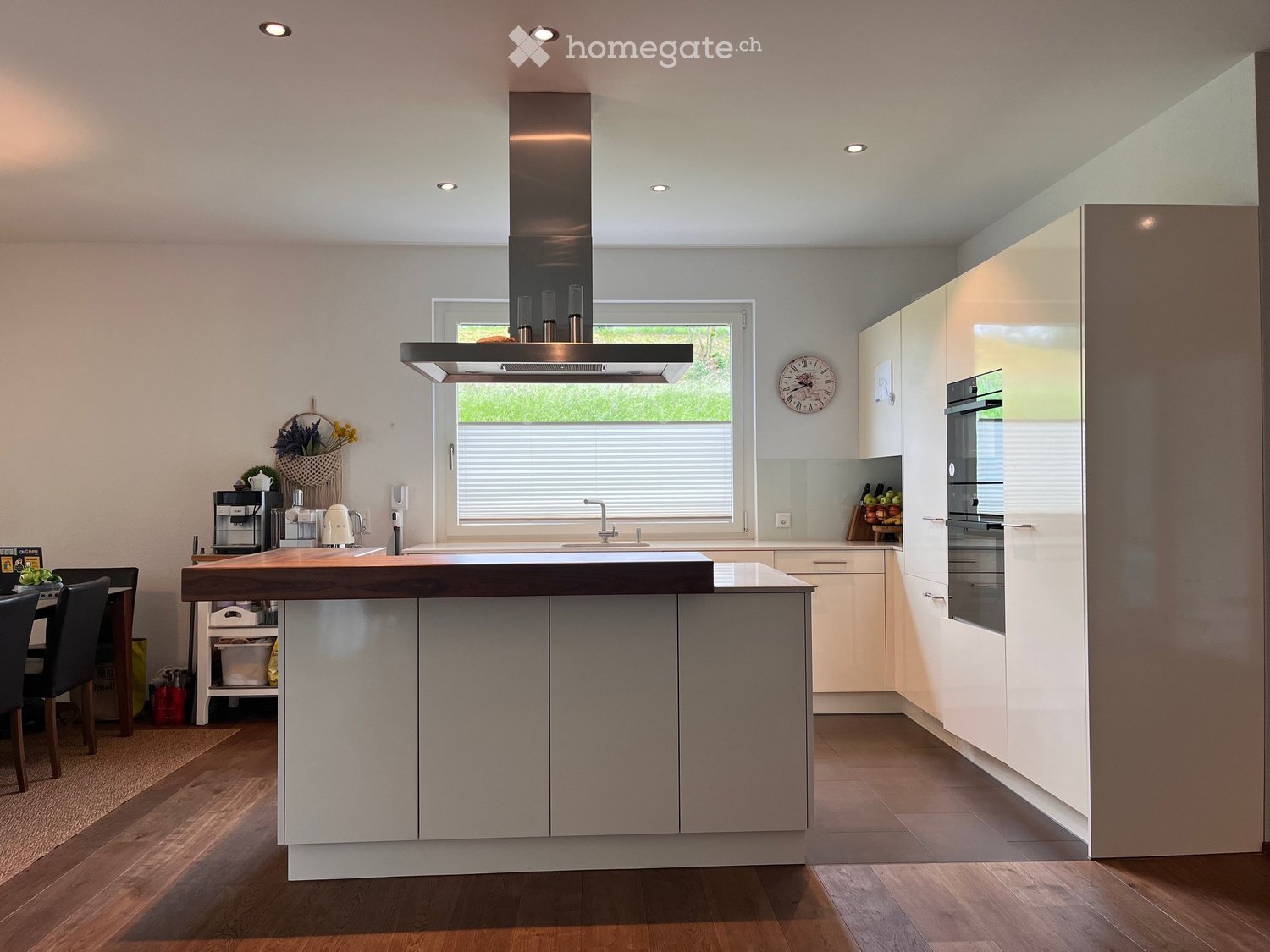 Modern kitchen with a central island, built-in oven, coffee maker, and a window overlooking greenery.