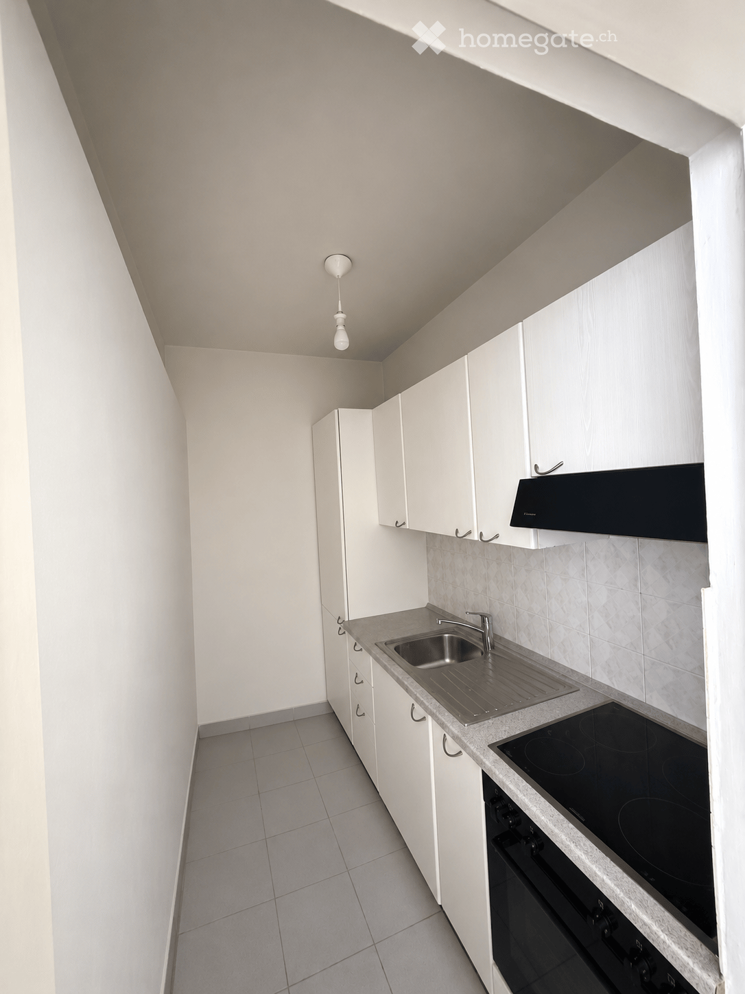 Modern kitchen with white cabinets, stainless steel sink, electric stove, and built-in oven. Light-colored tiles and a sleek design.